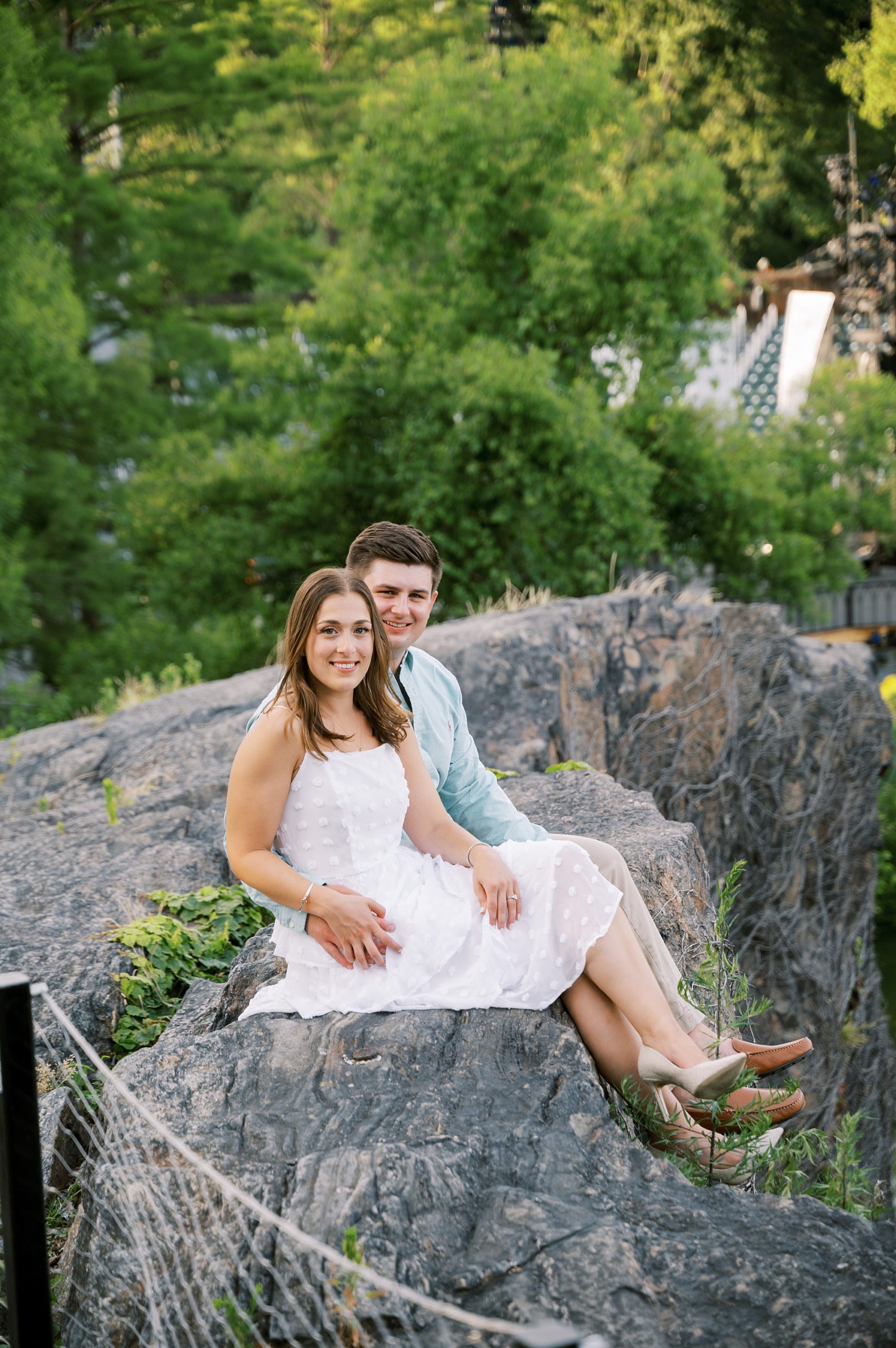 engaged couple sits on rocks by waterfront in Central Park