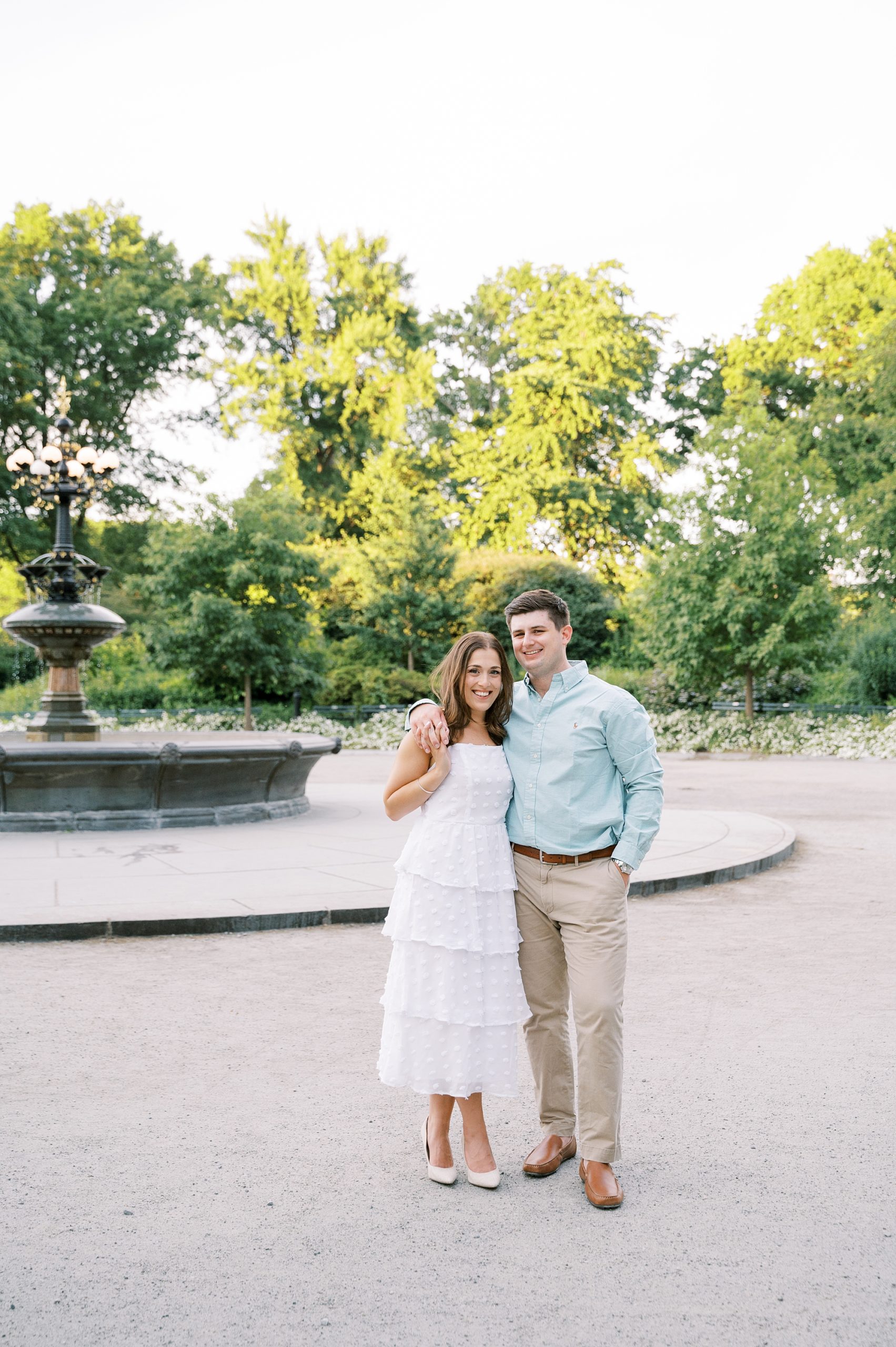 engaged couple in white dress and blue shirt pose by Bethesda Fountain