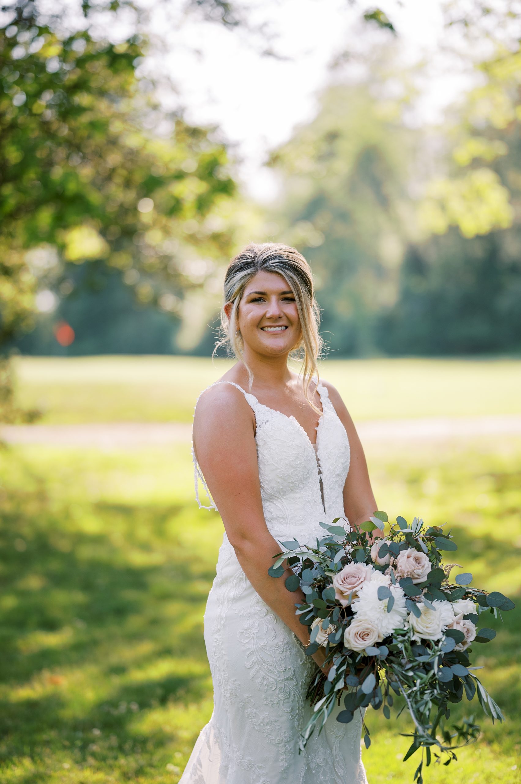 bride stands holding bouquet of ivory flowers for summer wedding