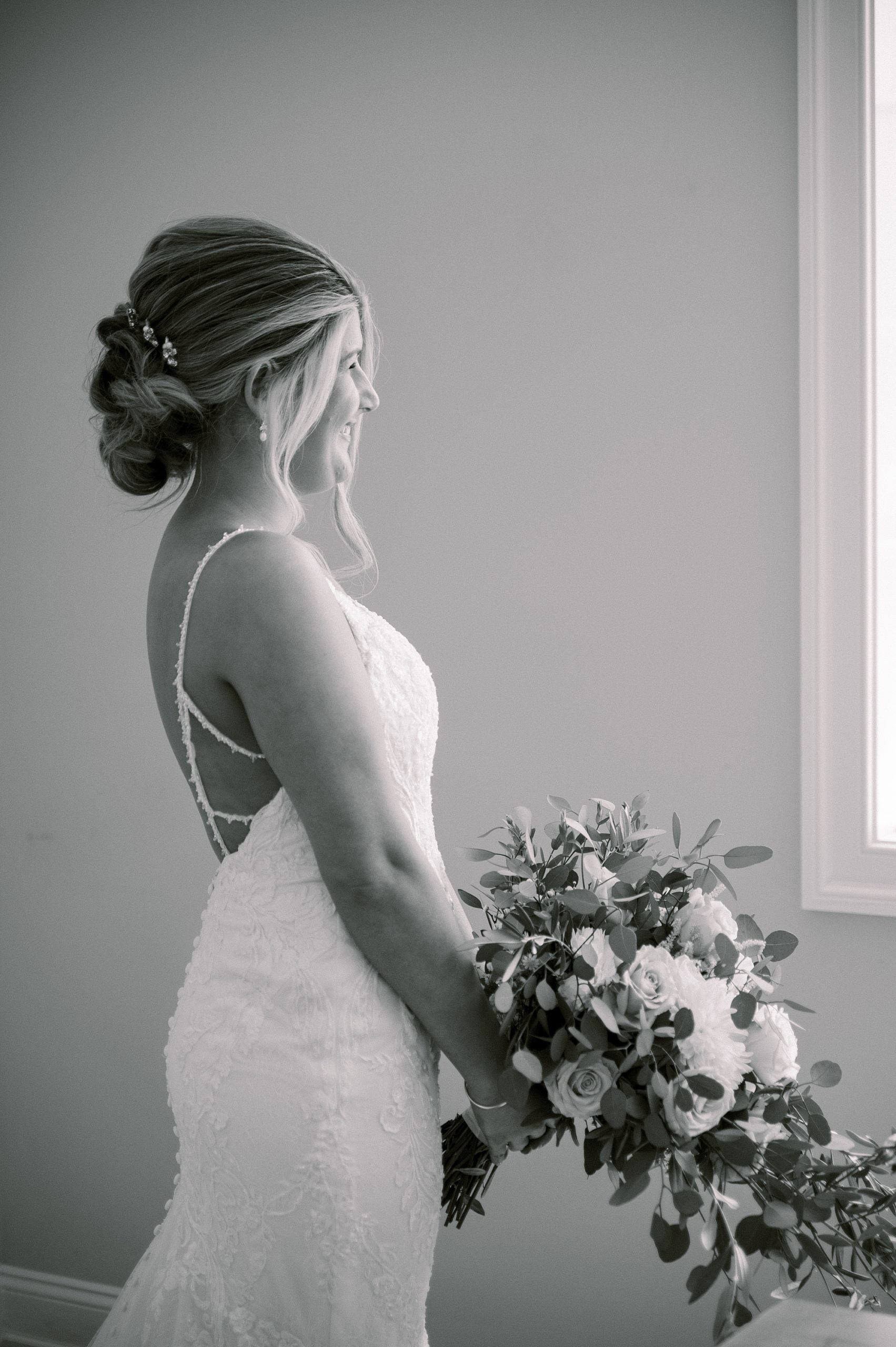 black and white portrait of bride holding bouquet looking out window at The Grove at Centerton