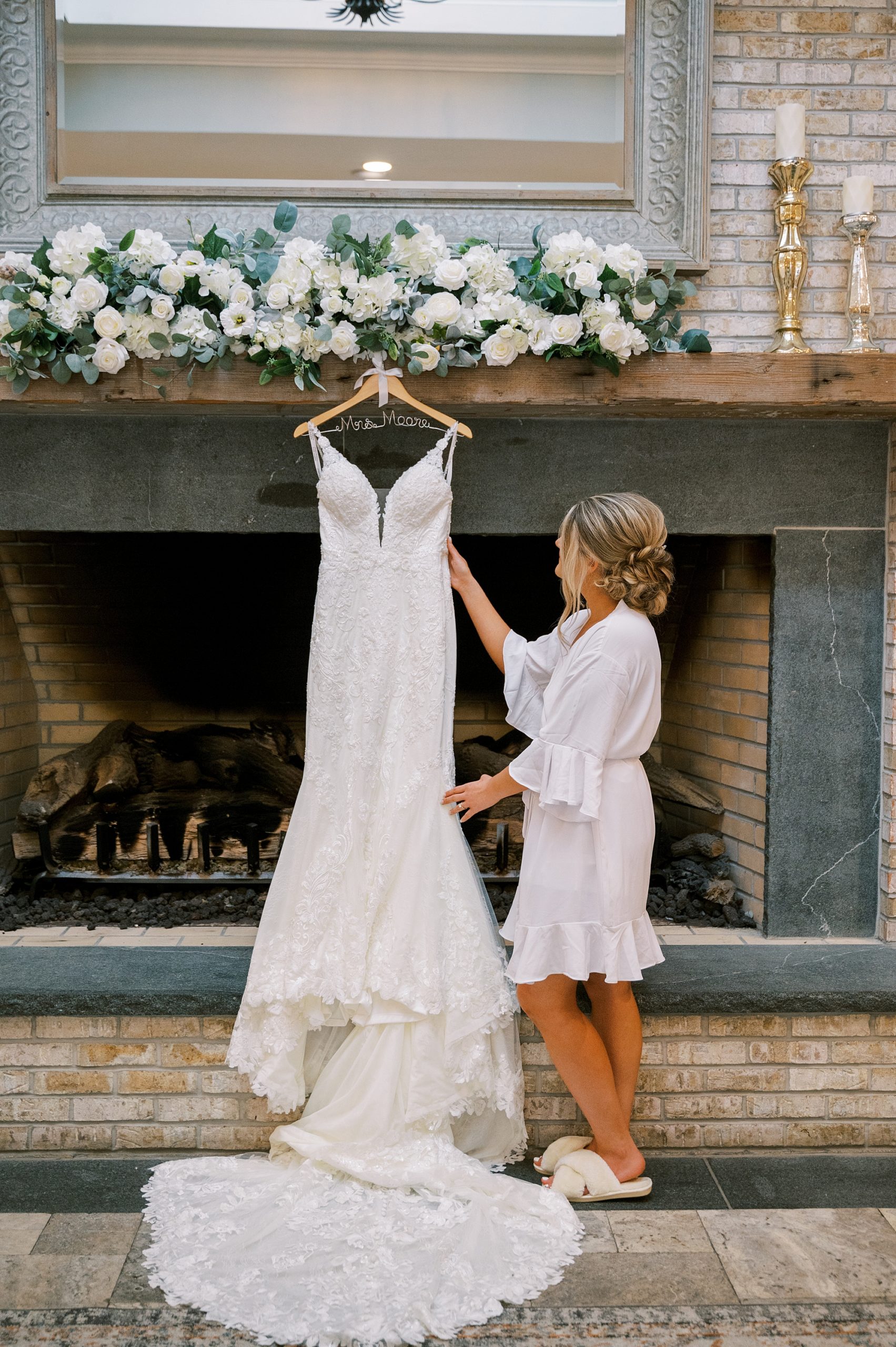 bride looks at wedding dress hanging on fireplace at The Grove at Centerton