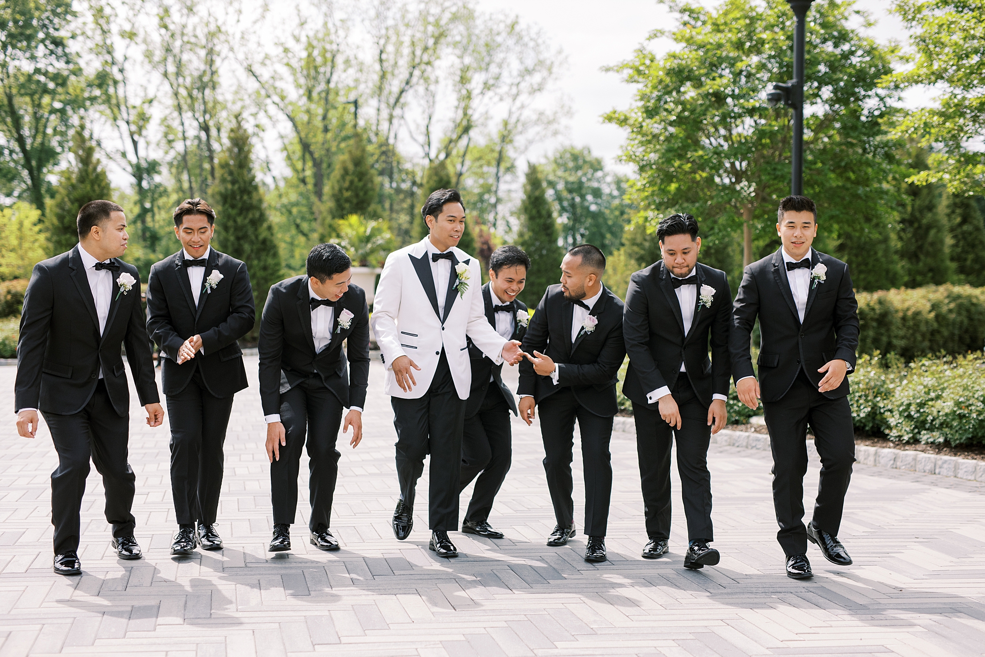 groom in white tux jacket walks with six groomsmen in black tuxes