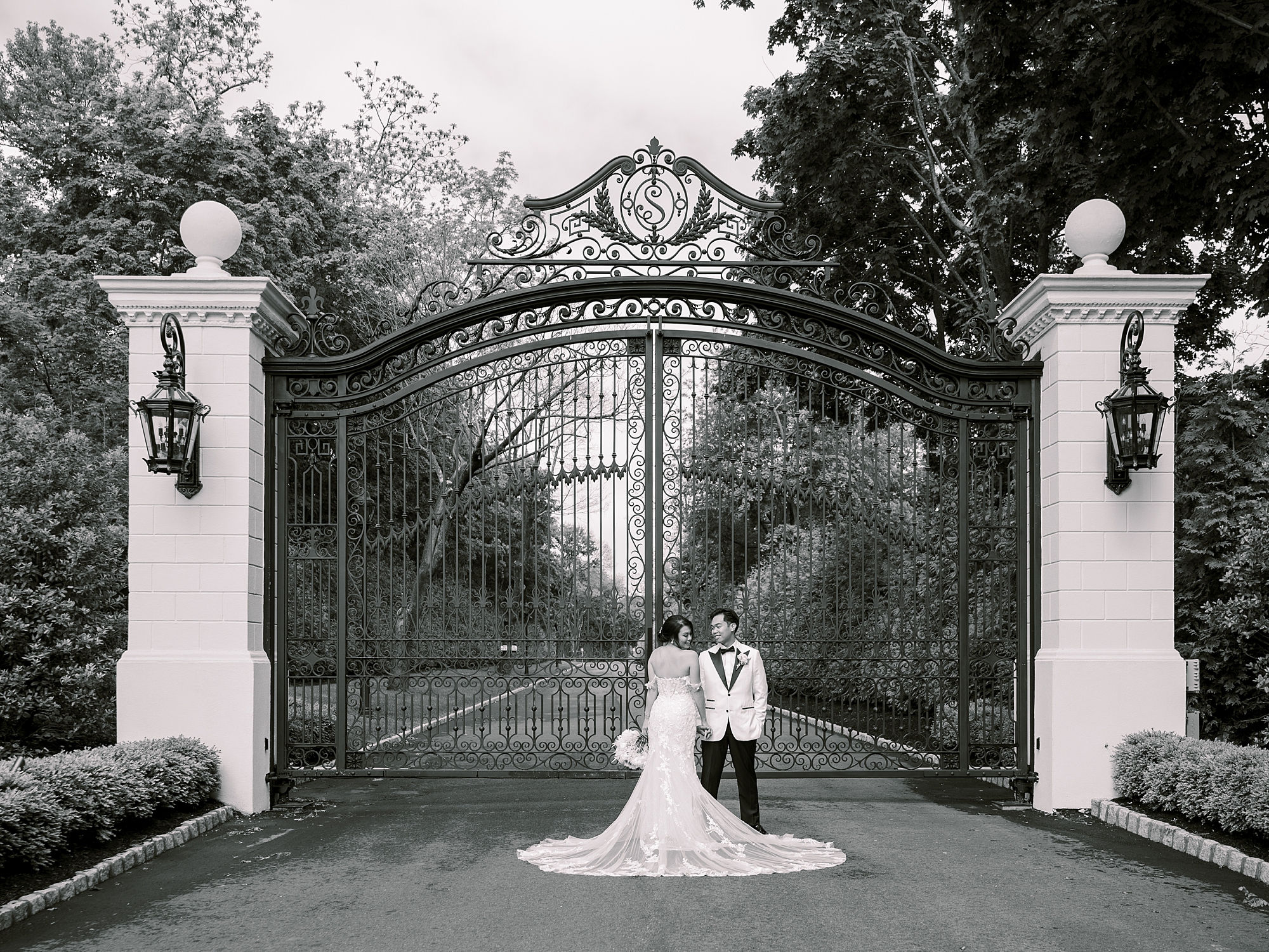 bride and groom pose by gates of Shadowbrook at Shrewsbury
