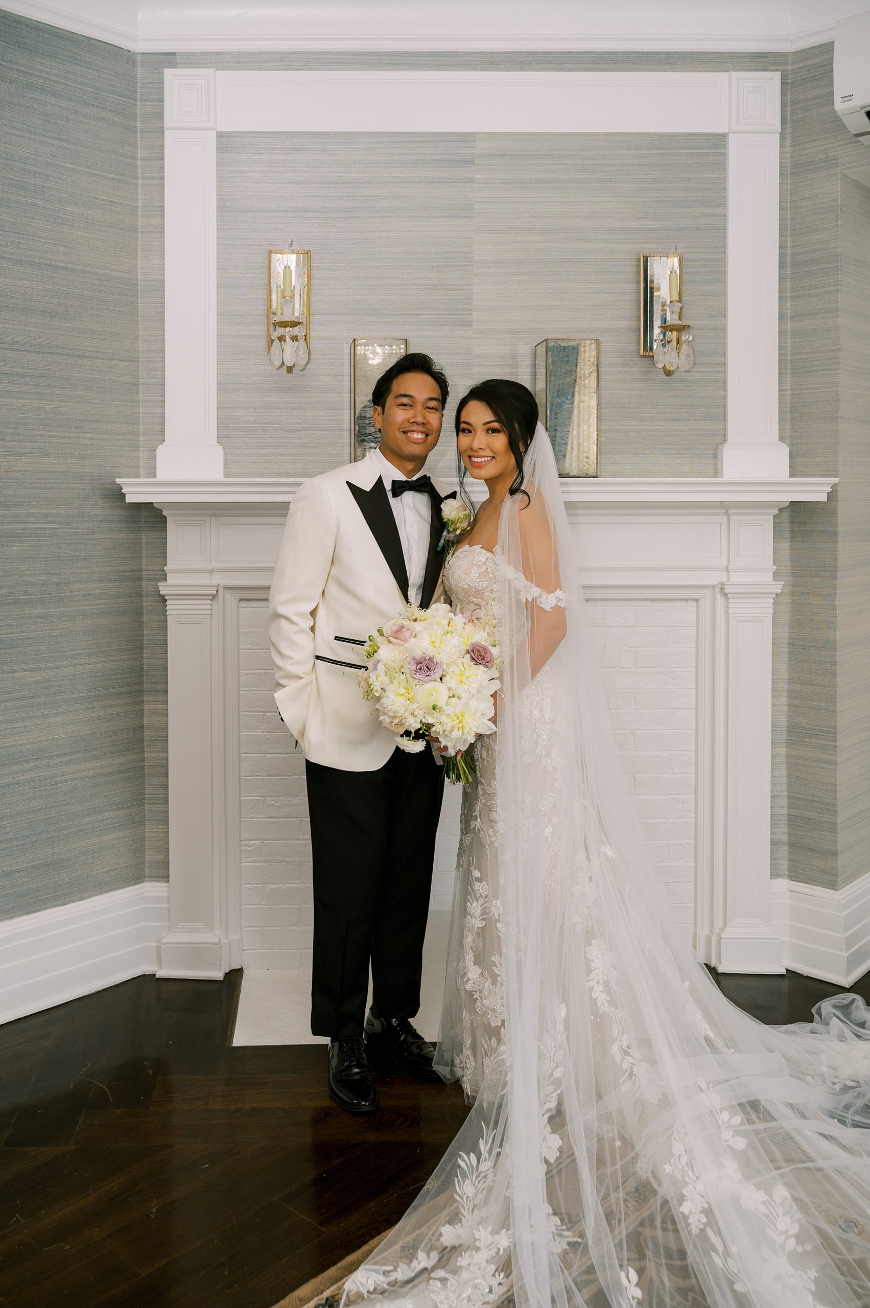 bride and groom stand by white fireplace inside Shadowbrook at Shrewsbury