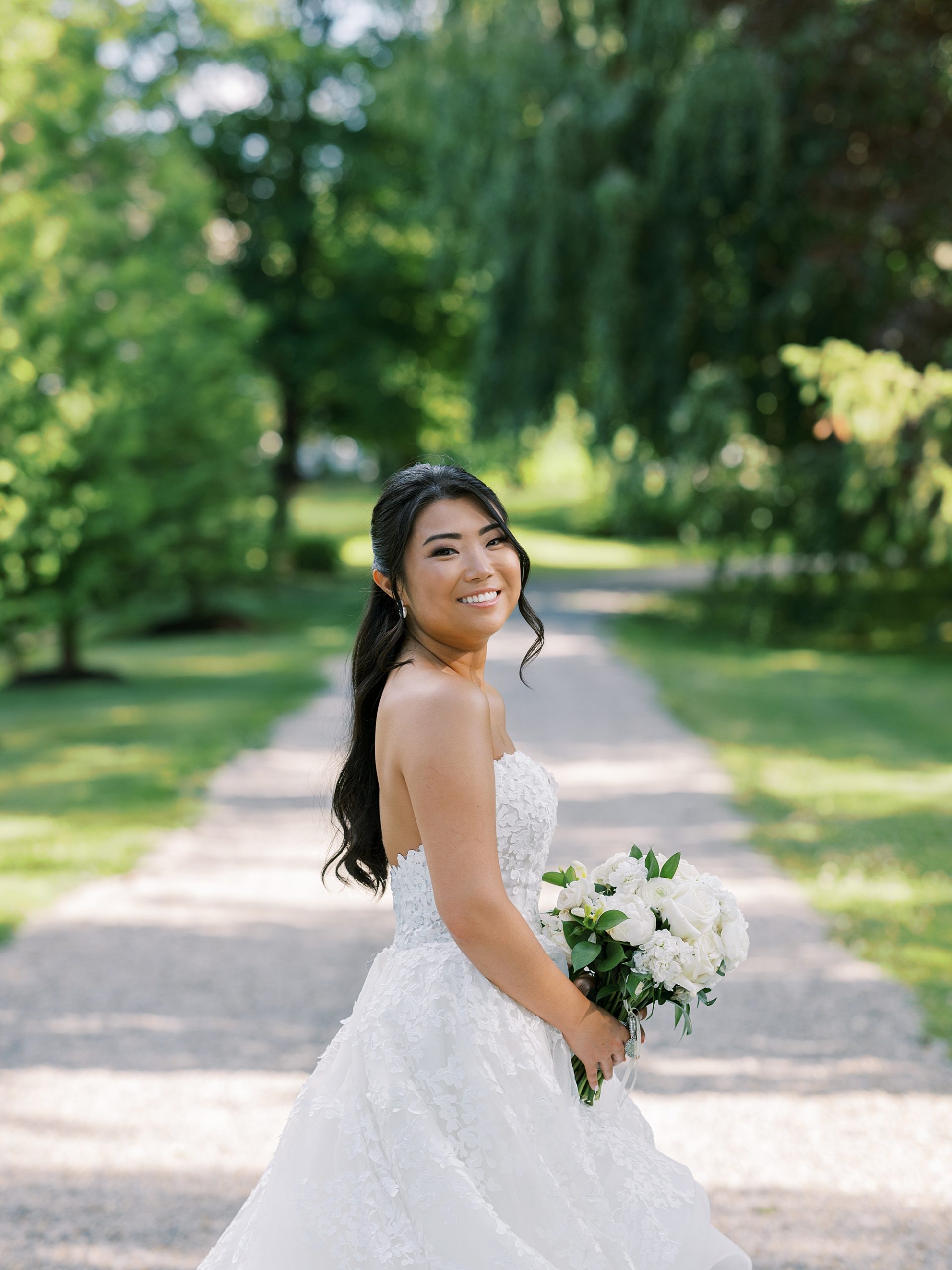bride smiles looking over shoulder in wedding gown with small bouquet of white flowers
