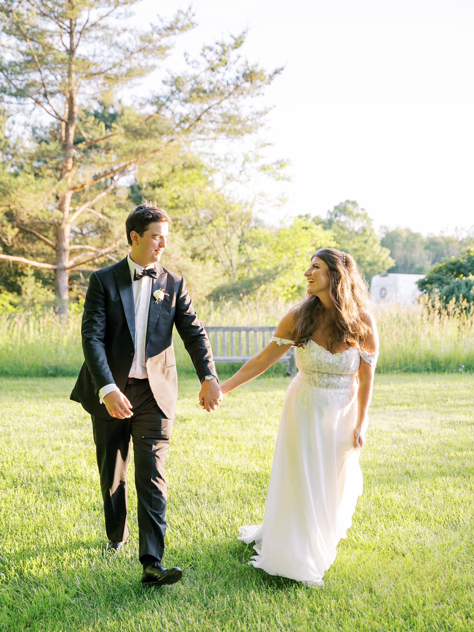 bride and groom hold hands walking through field in Willowwood Arboretum