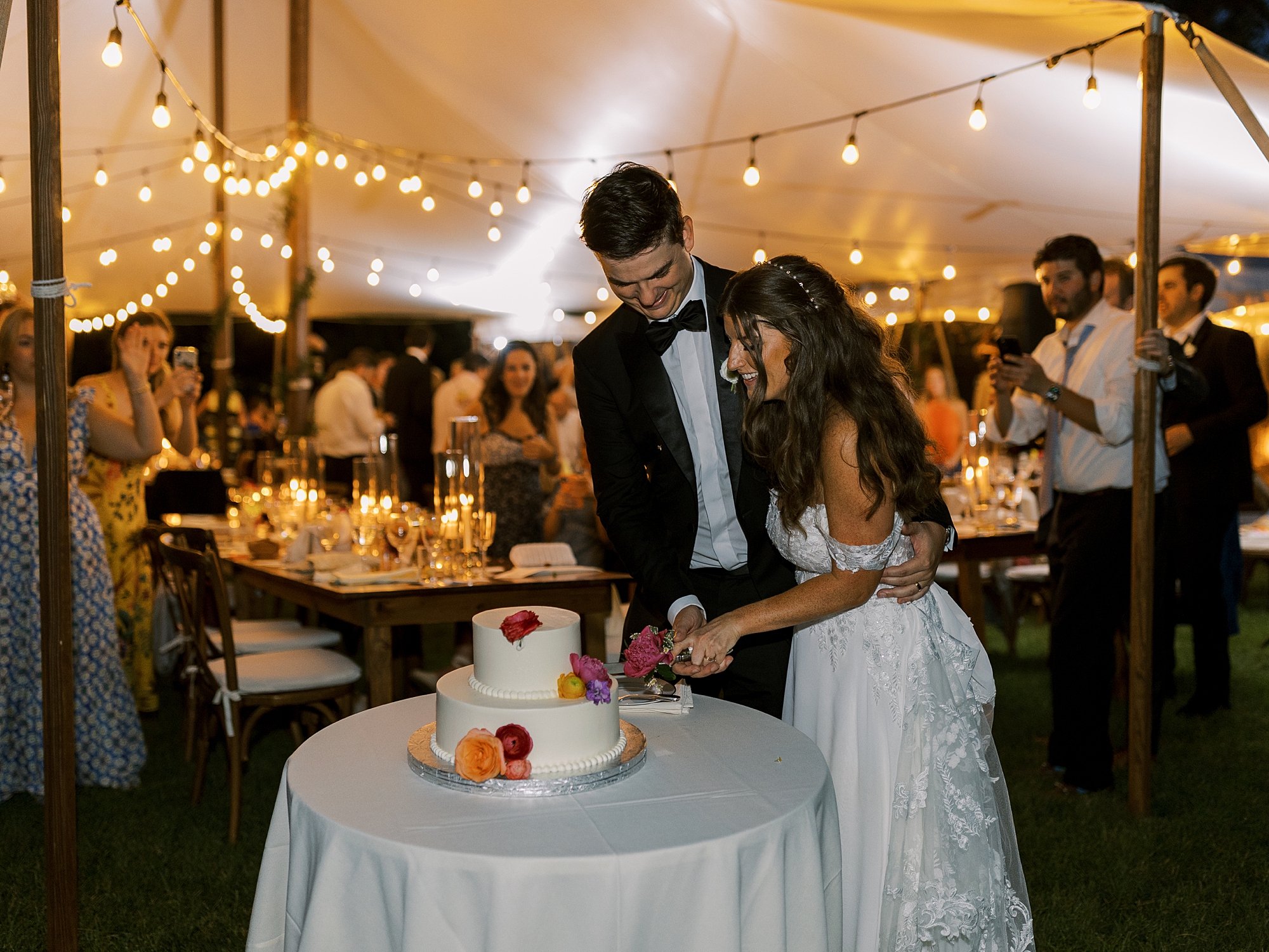 newlyweds cut wedding cake under tent at Willowwood Arboretum
