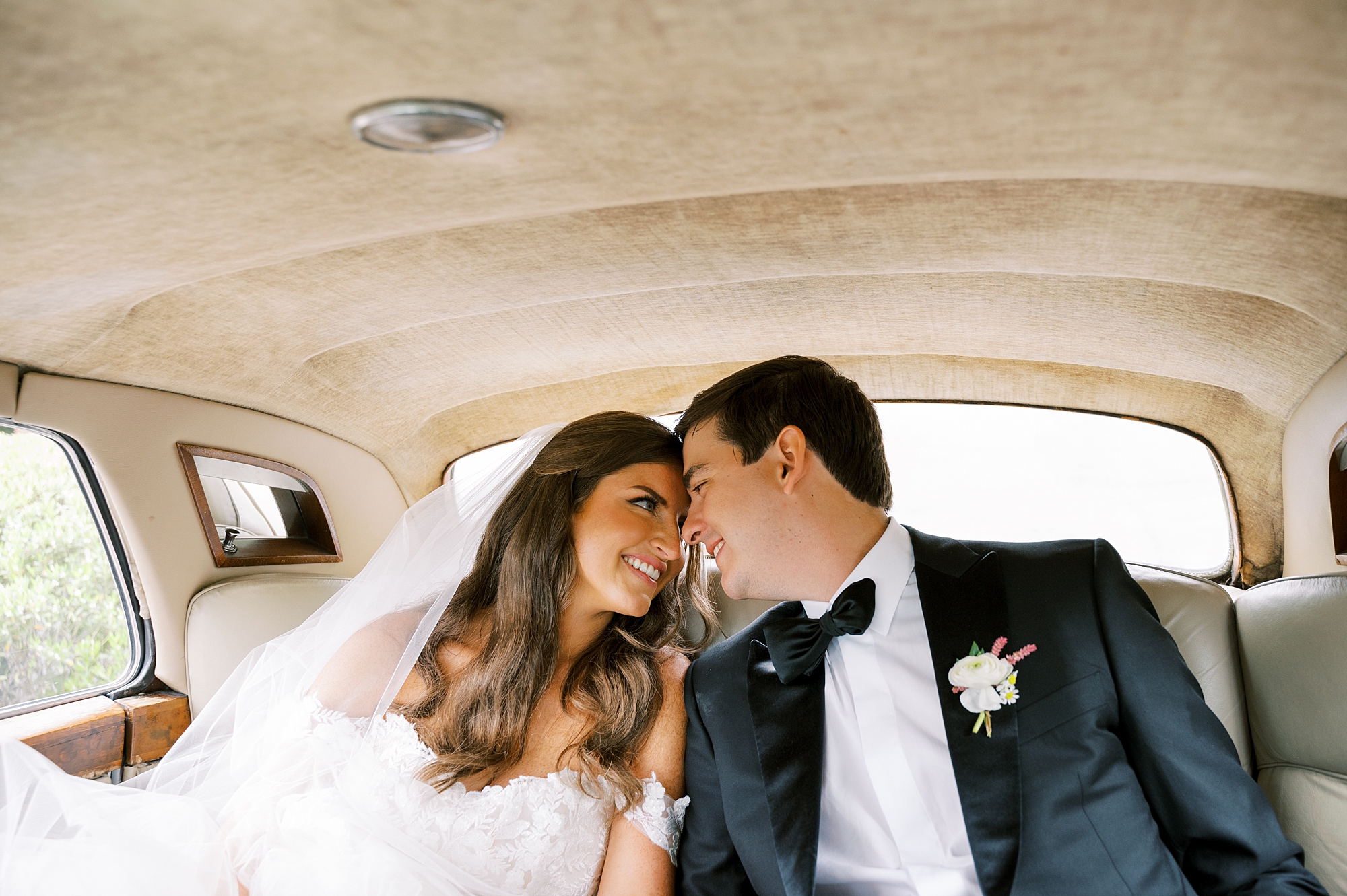 bride and groom in black tux lean heads together in classic car