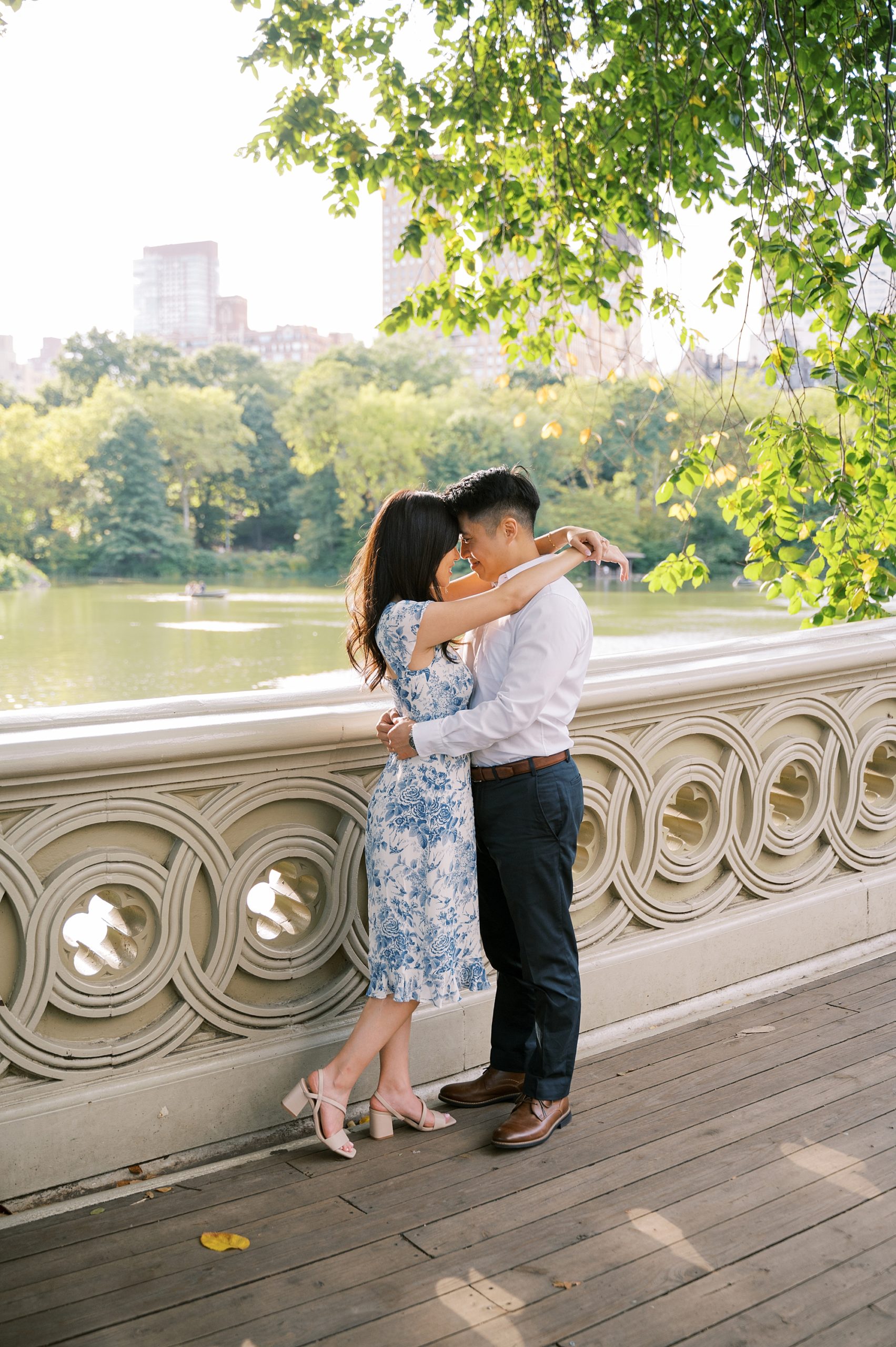 woman stands on bridge hugging fiancee in Central Park