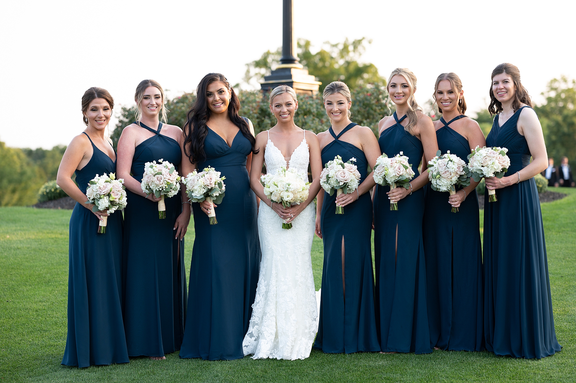 bride poses with bridesmaids in navy gowns with white flowers 