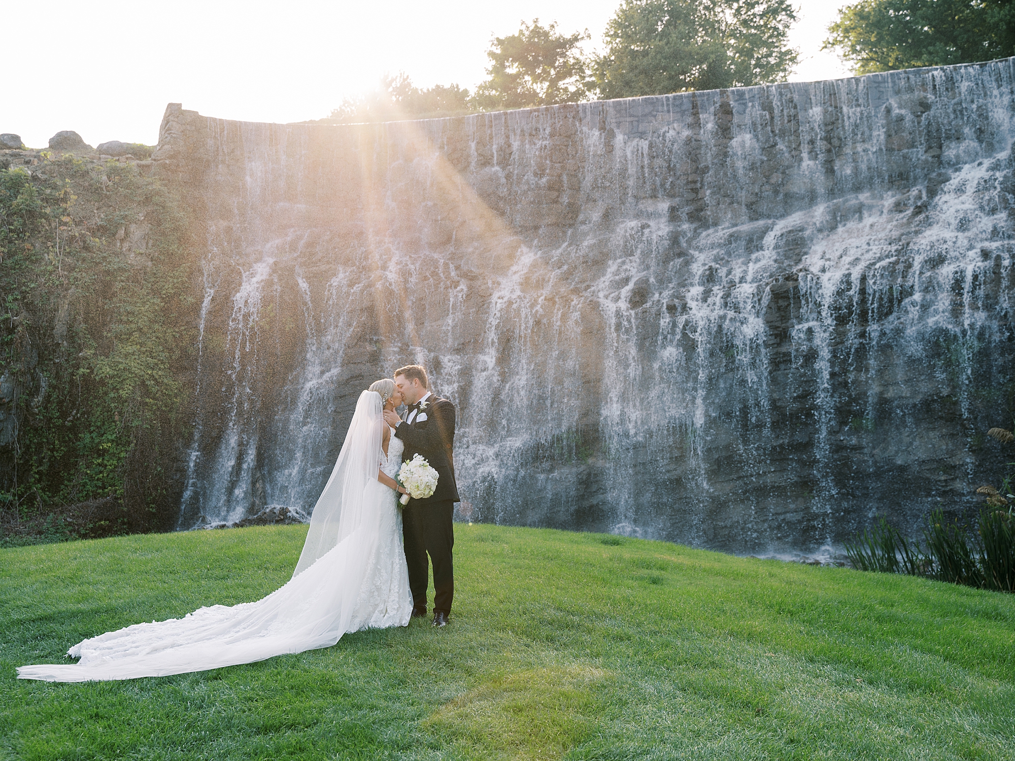 bride and groom kiss by waterfall display at Trump National Golf Club Westchester
