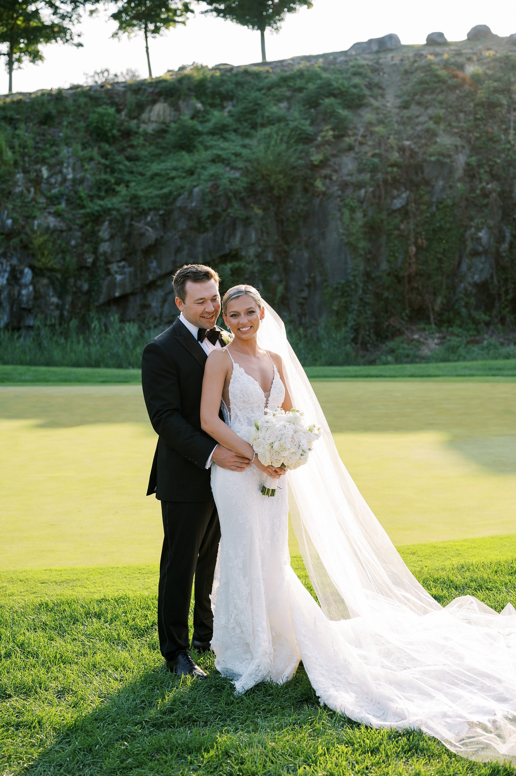 groom hugs bride from behind on green at Trump National Golf Club WestchesterTrump National Golf Club Westchester