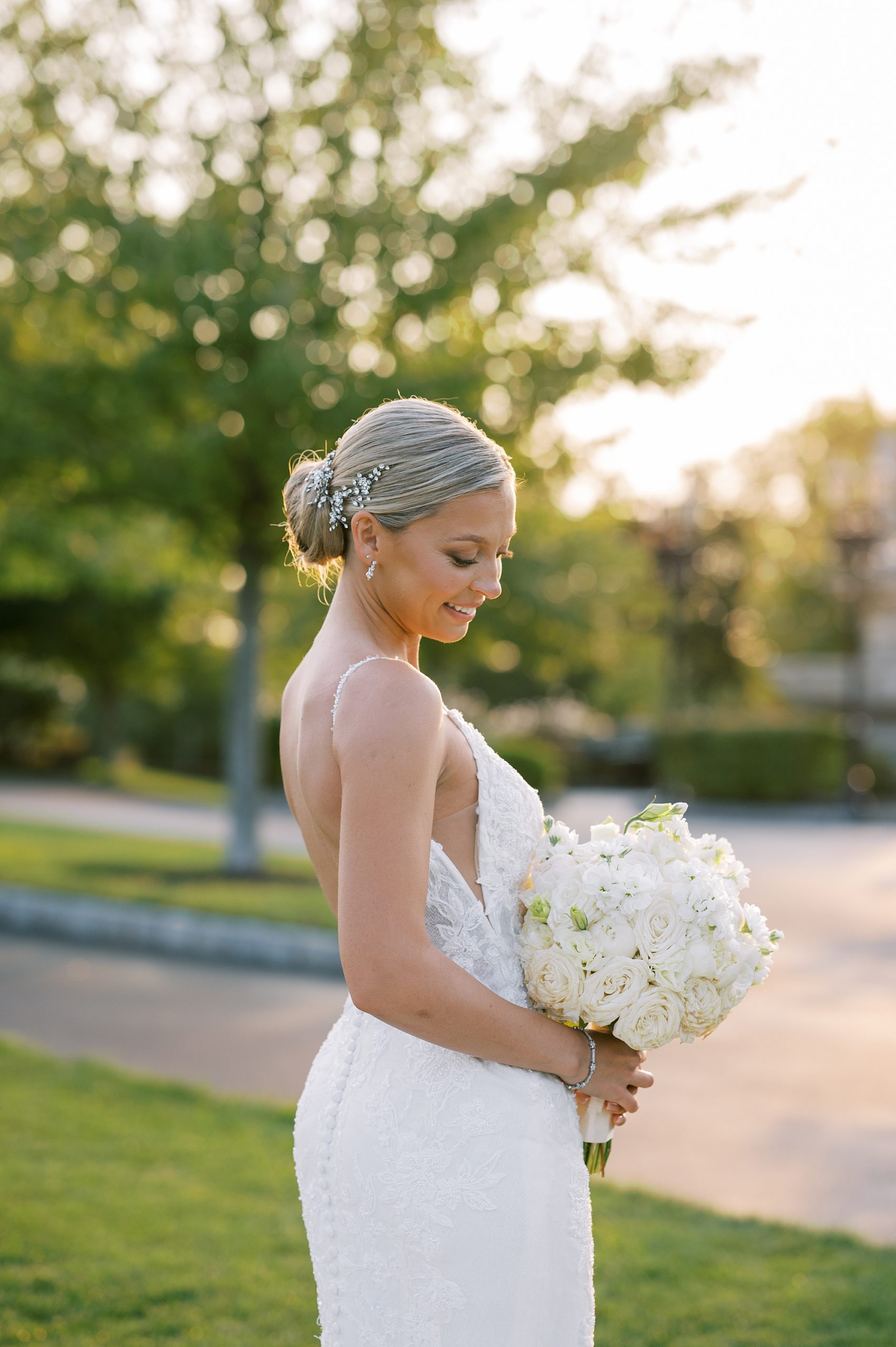 bride with hair in updo smiles down at bouquet of ivory flowers 