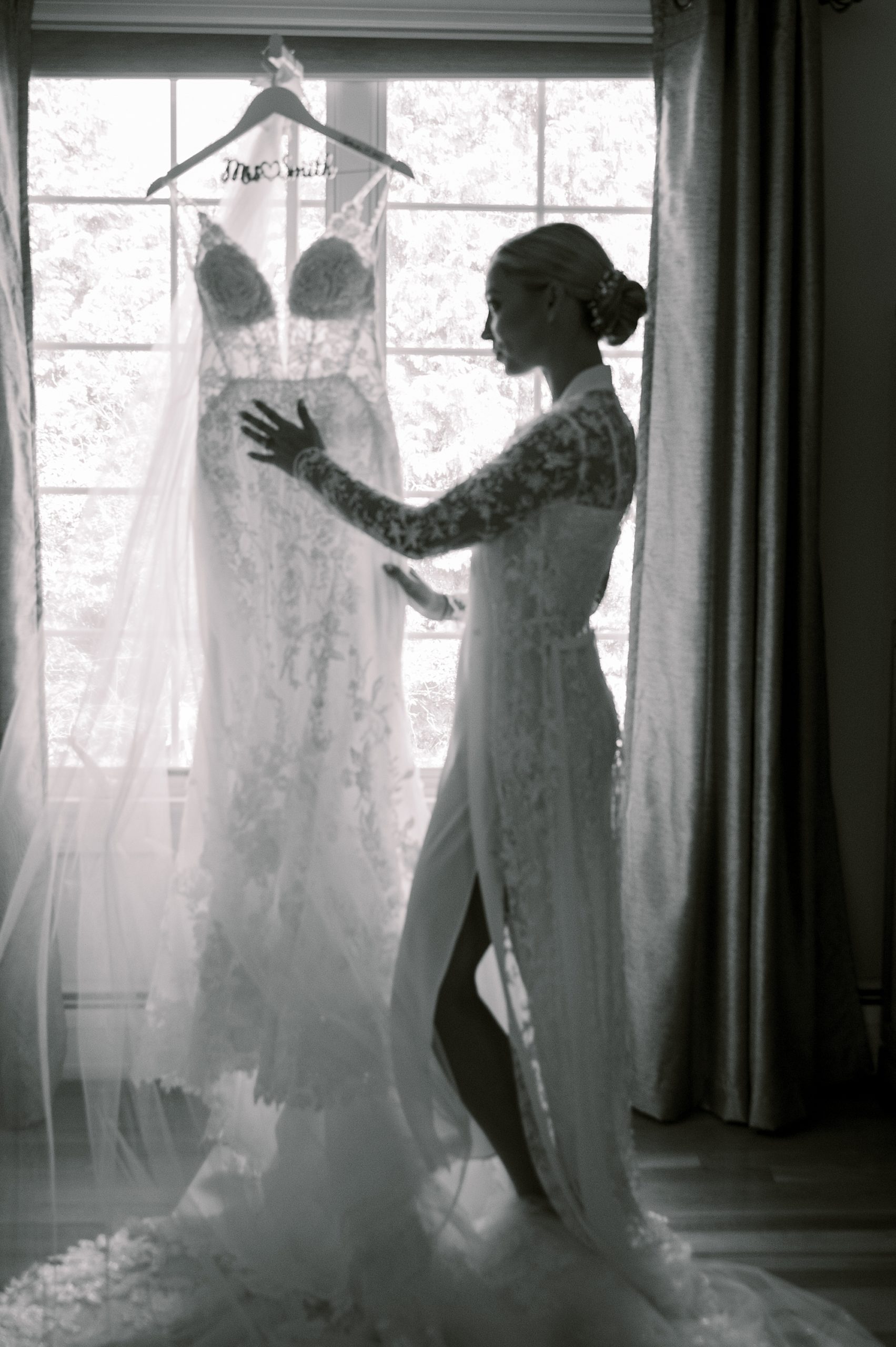 black and white portrait of bride looking at wedding gown in window 