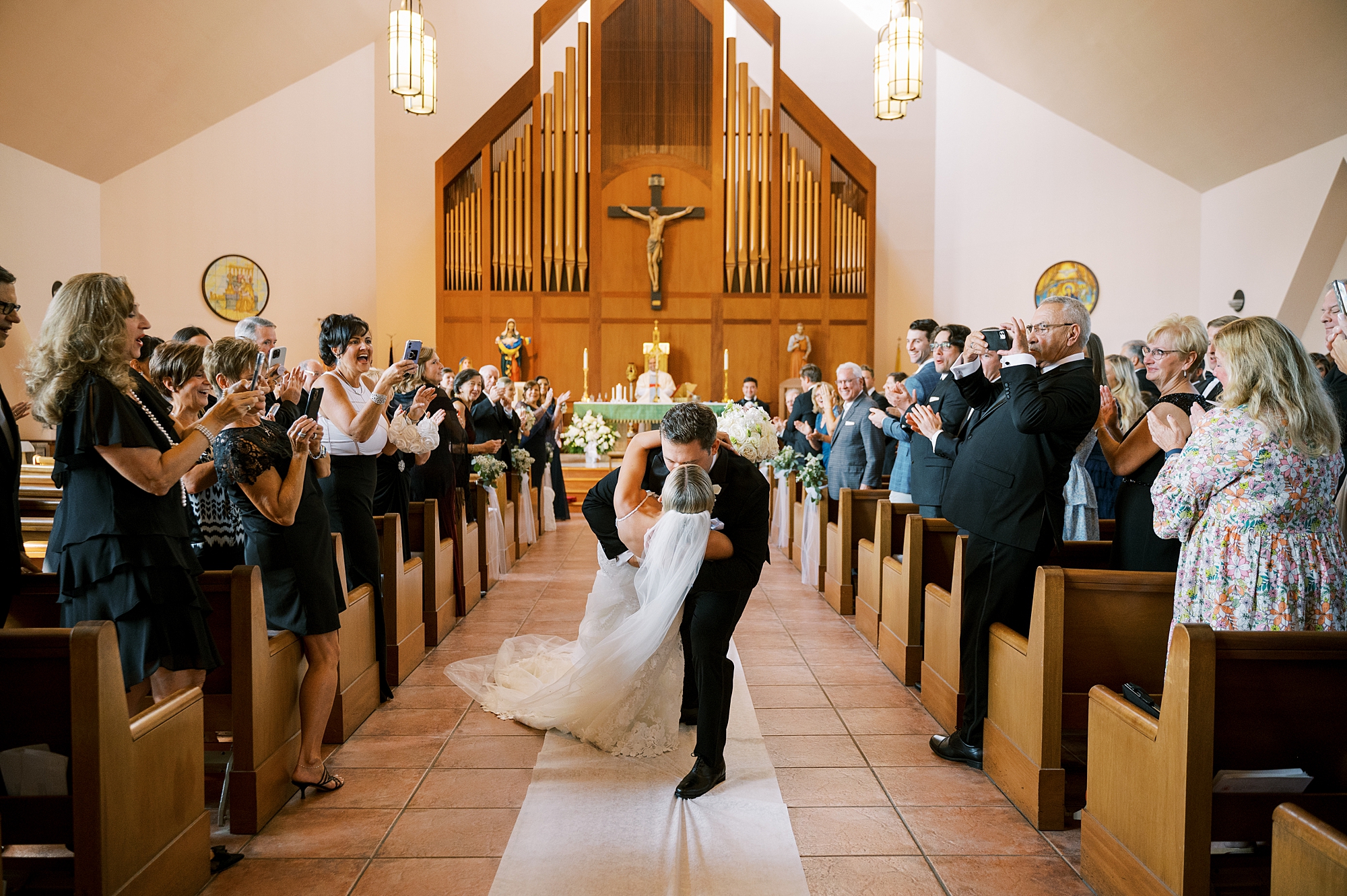 groom dips bride kissing her in aisle after traditional Catholic Church wedding at St. Augustine Catholic Church
