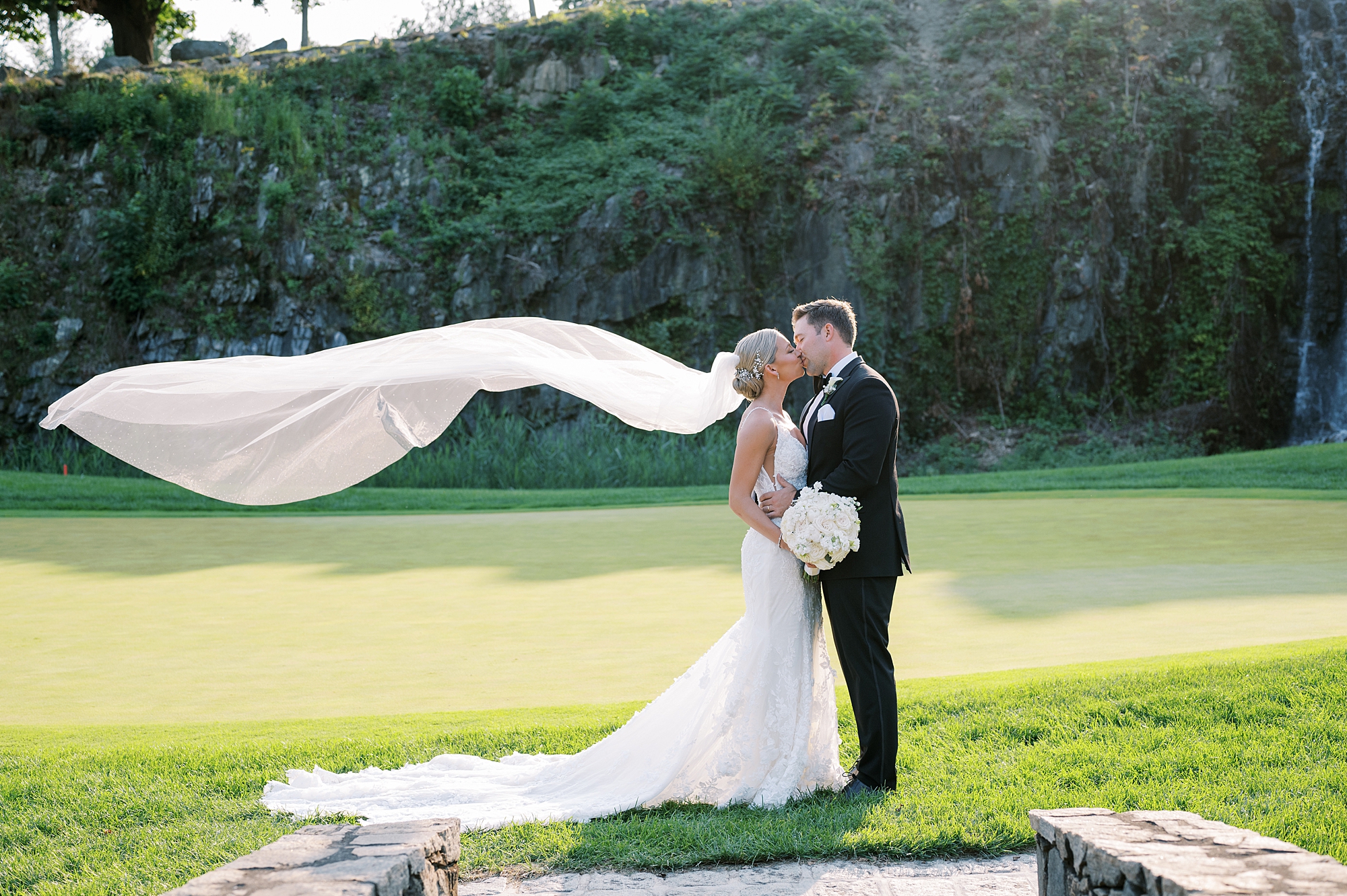 groom kisses bride while veil floats behind them at  Trump National Golf Club Westchester