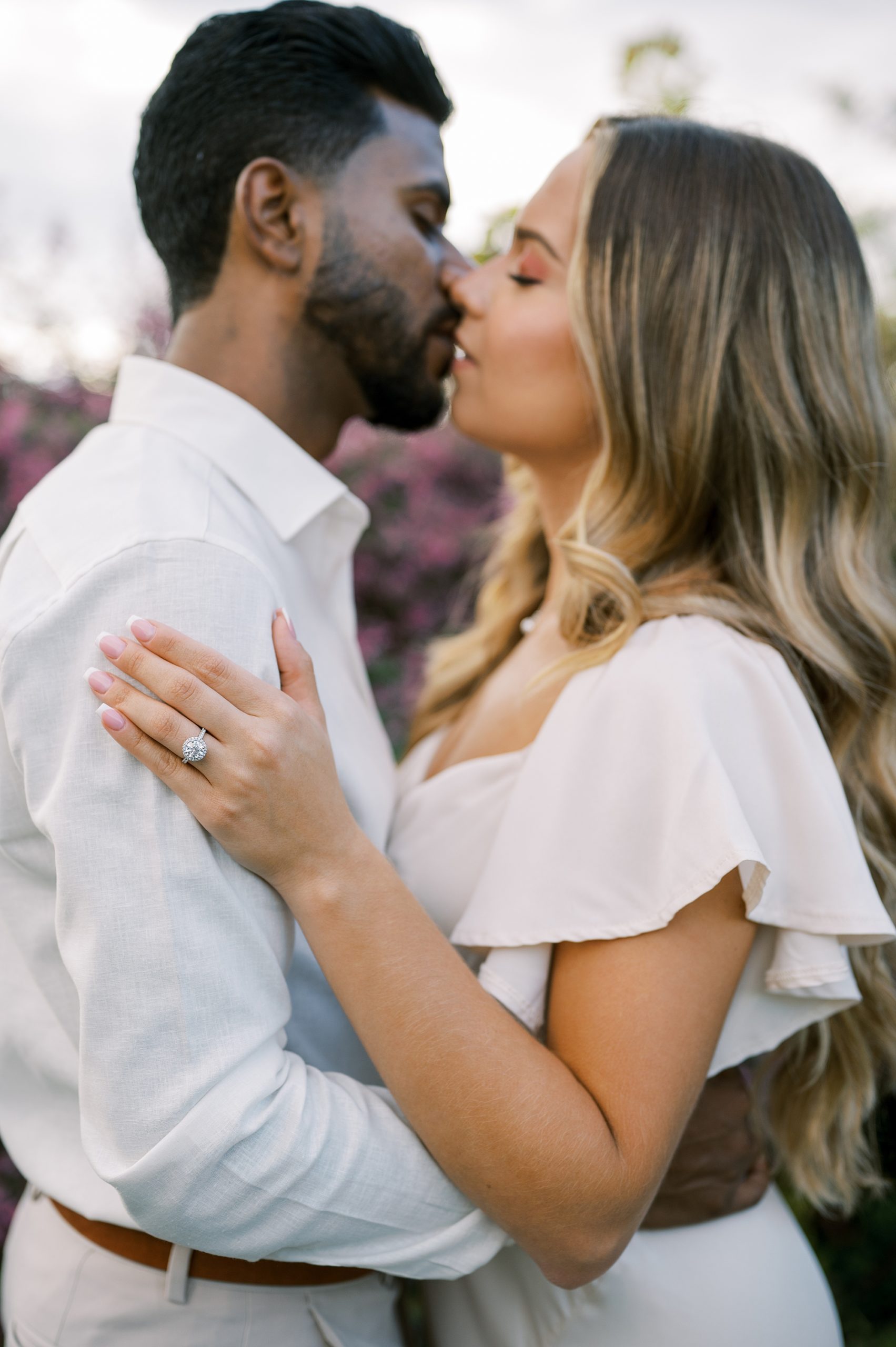 couple kisses while bride holds groom's bicep showing off ring