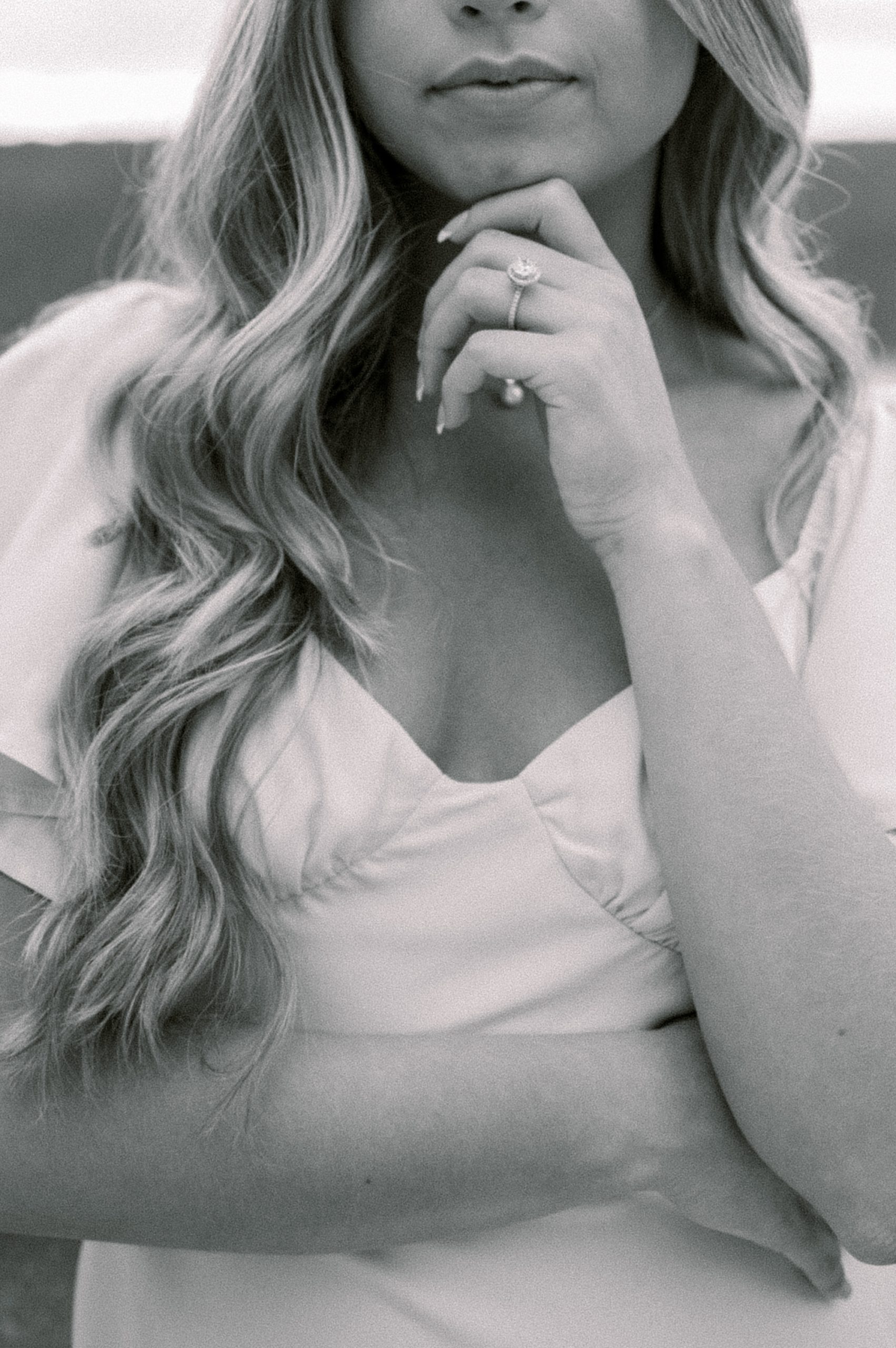 black and white portrait of bride in white dress with hand against chin showing off engagement ring