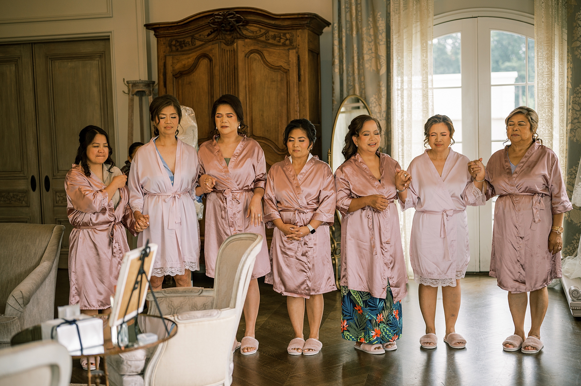 bridesmaids in pink robes stand inside bridal suite with eyes shut at Park Chateau