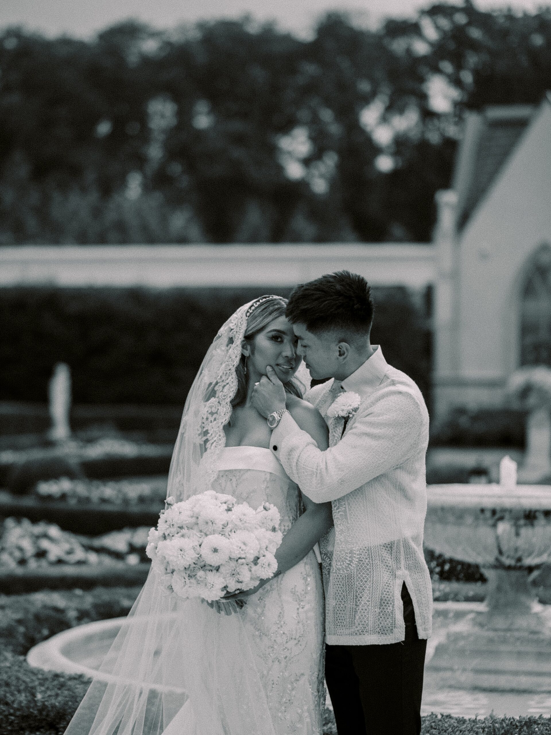 groom hugs bride holding her chin in front of fountain at Park Chateau Estate