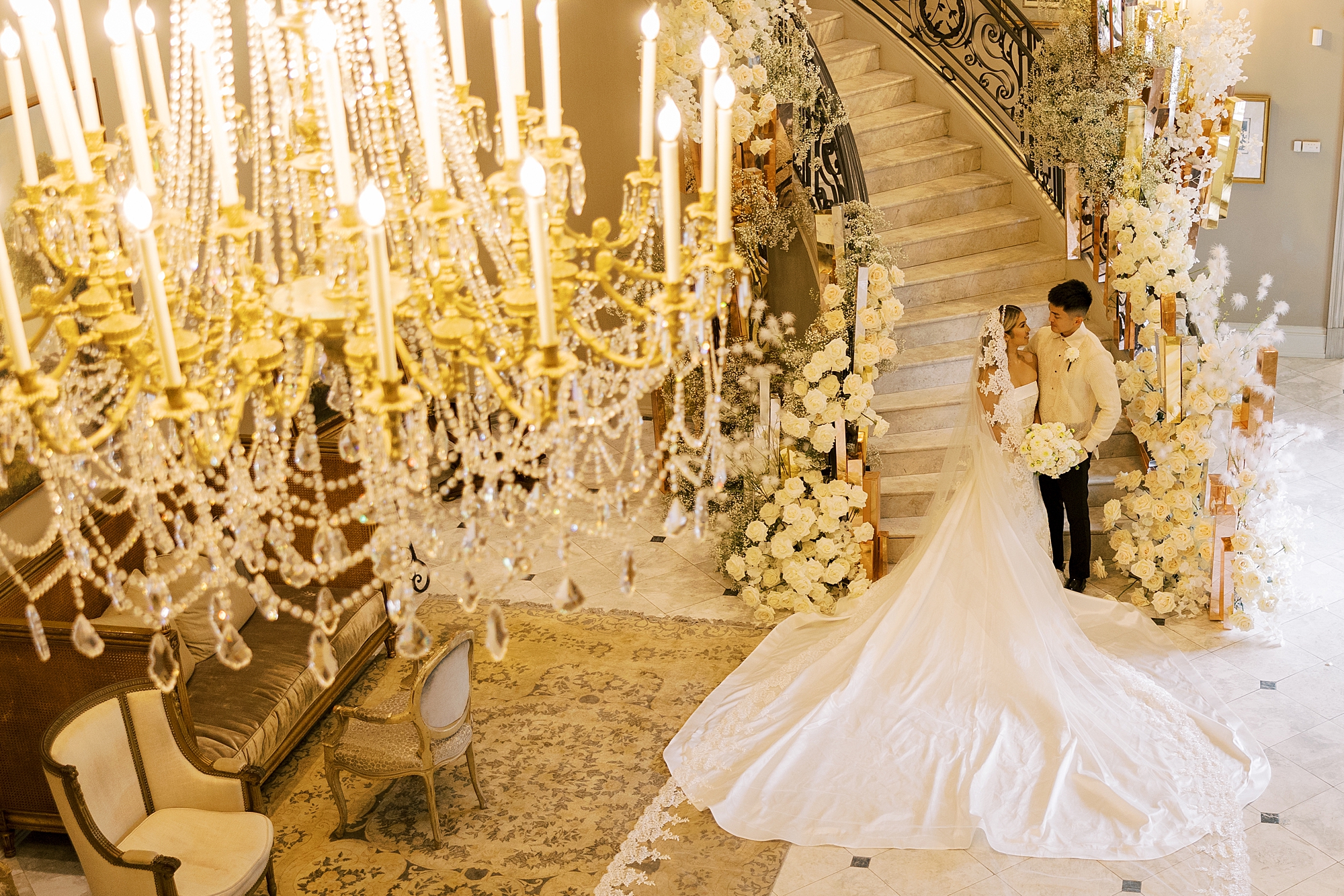 newlyweds stand on staircase inside Park Chateau Estate with white candle and florals around them