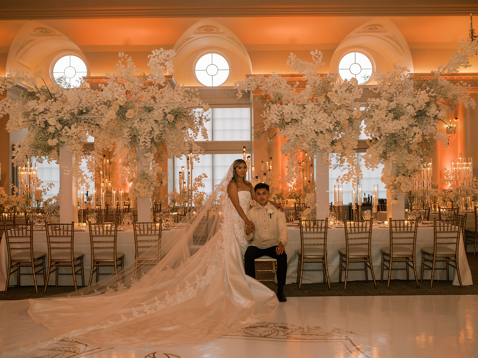 groom sits in chair with bride on his knee inside Park Chateau Estate ballroom