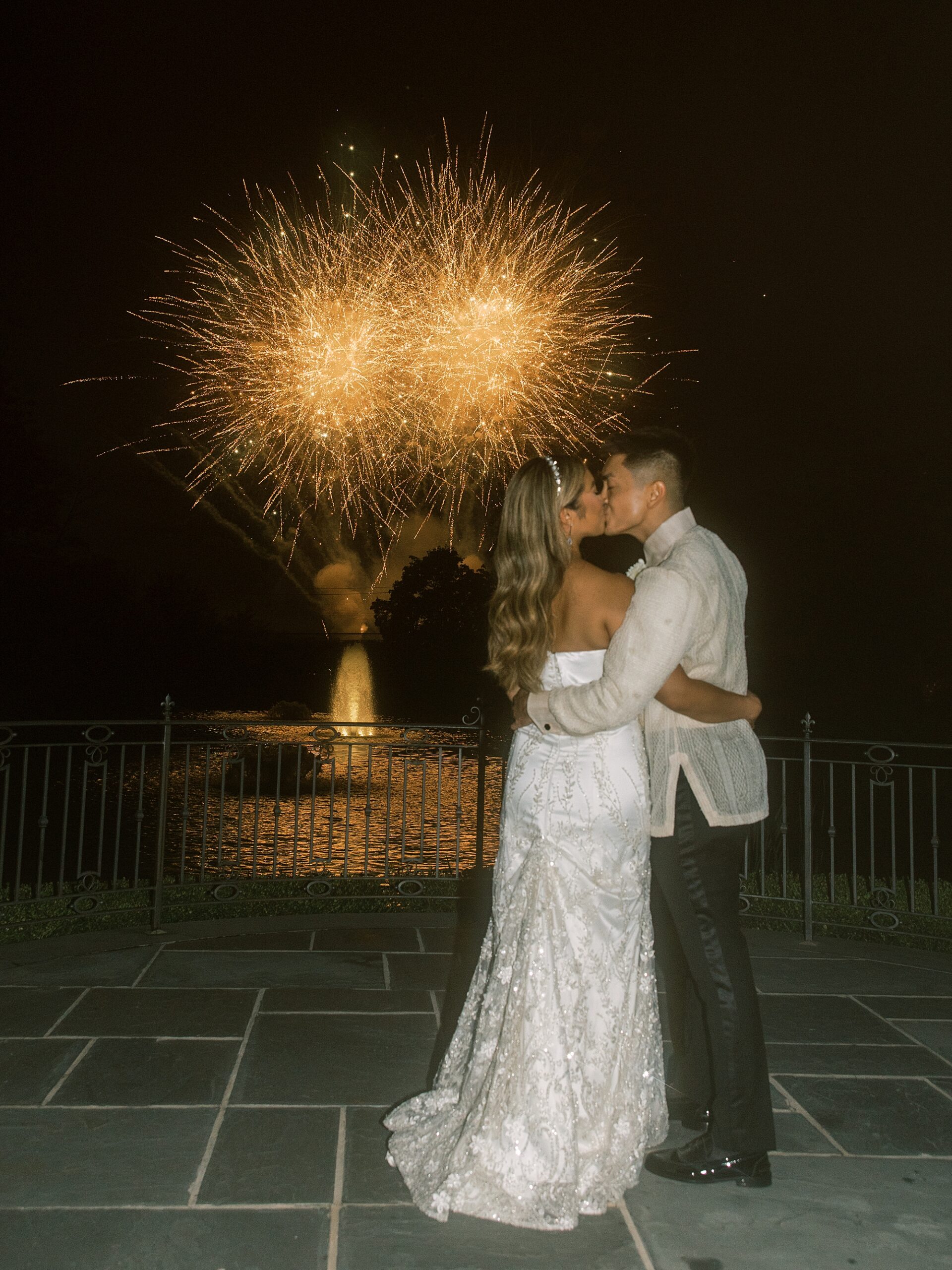 bride and groom kiss on balcony at Park Chateau Estate with fireworks behind them