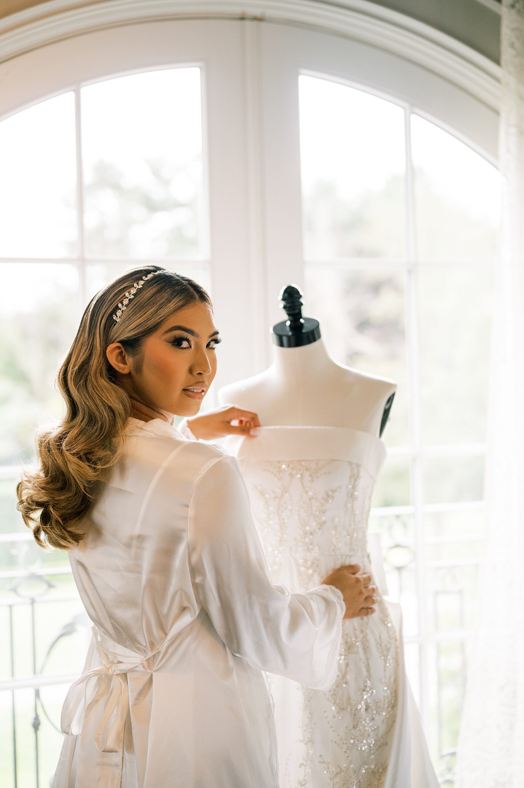 bride smiles over shoulder looking at wedding gown on mannequin 