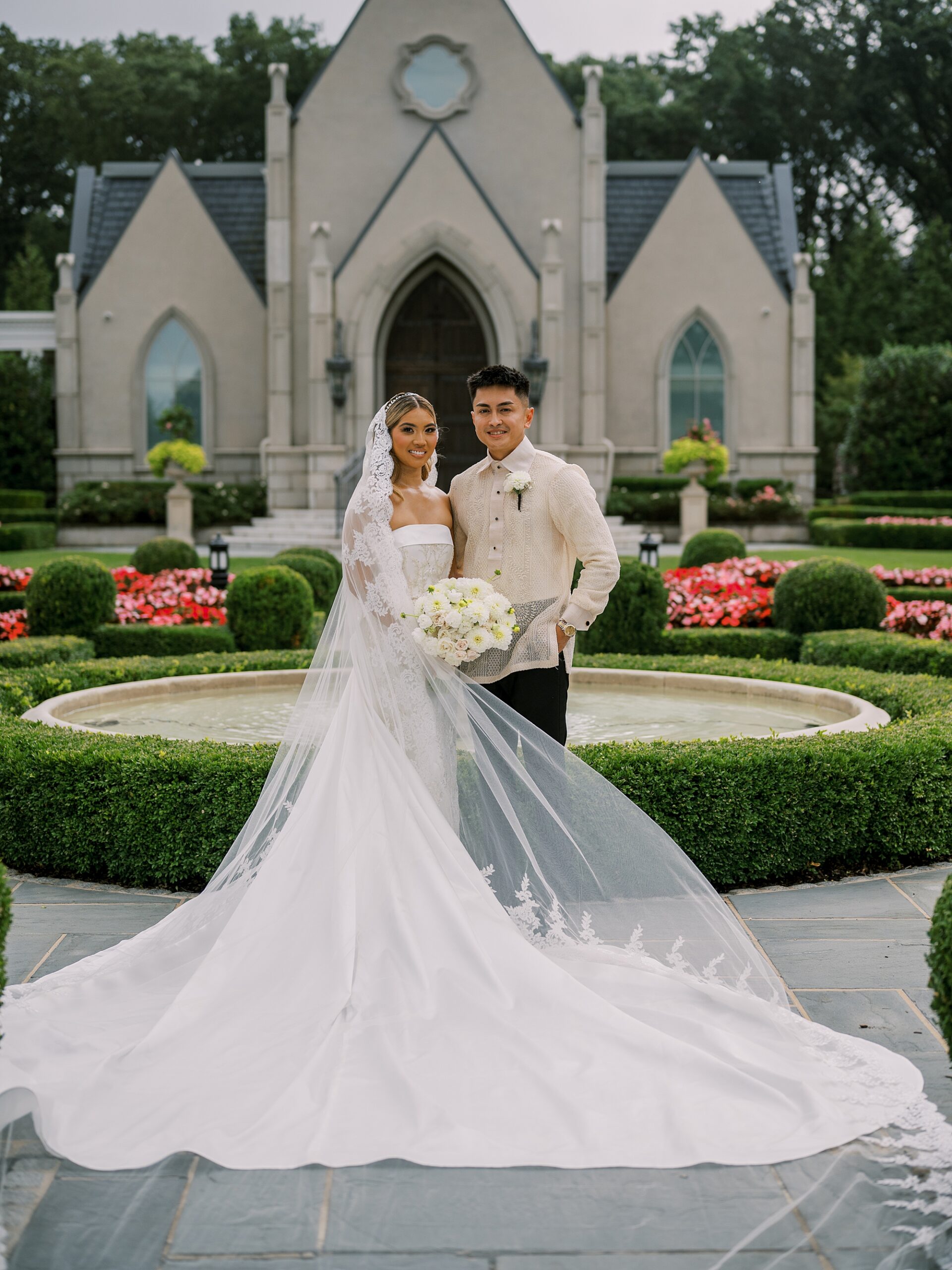 newlyweds stand in gardens outside Park Chateau Estate chapel