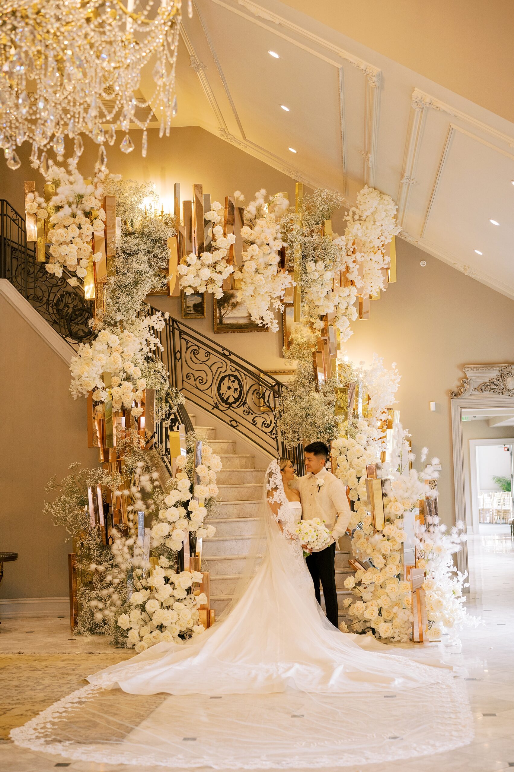 newlyweds pose at the end of the staircase inside Park Chateau Estate lined with ivory flowers