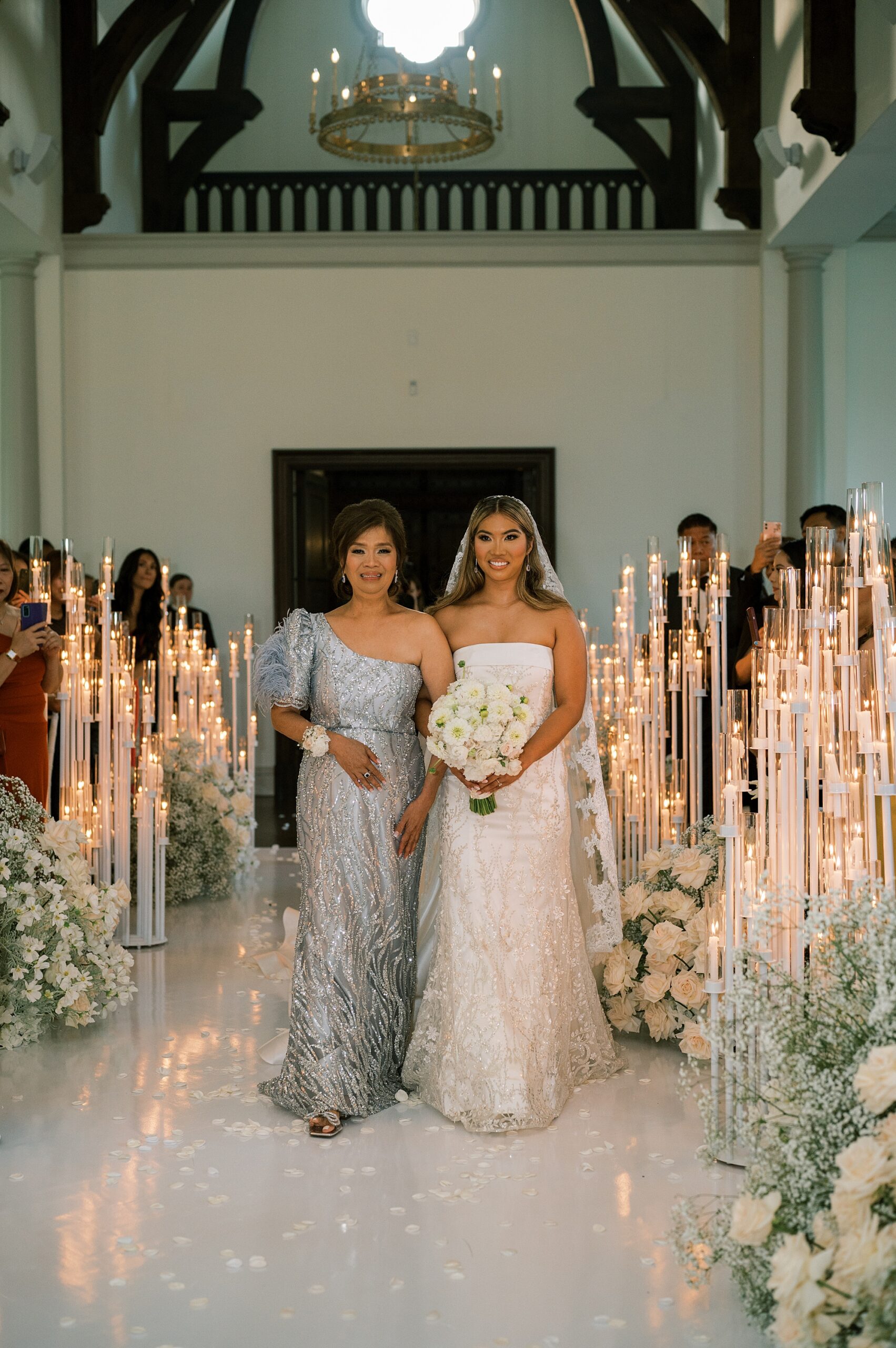 mother walks bride down aisle lined with tall white taper candles 