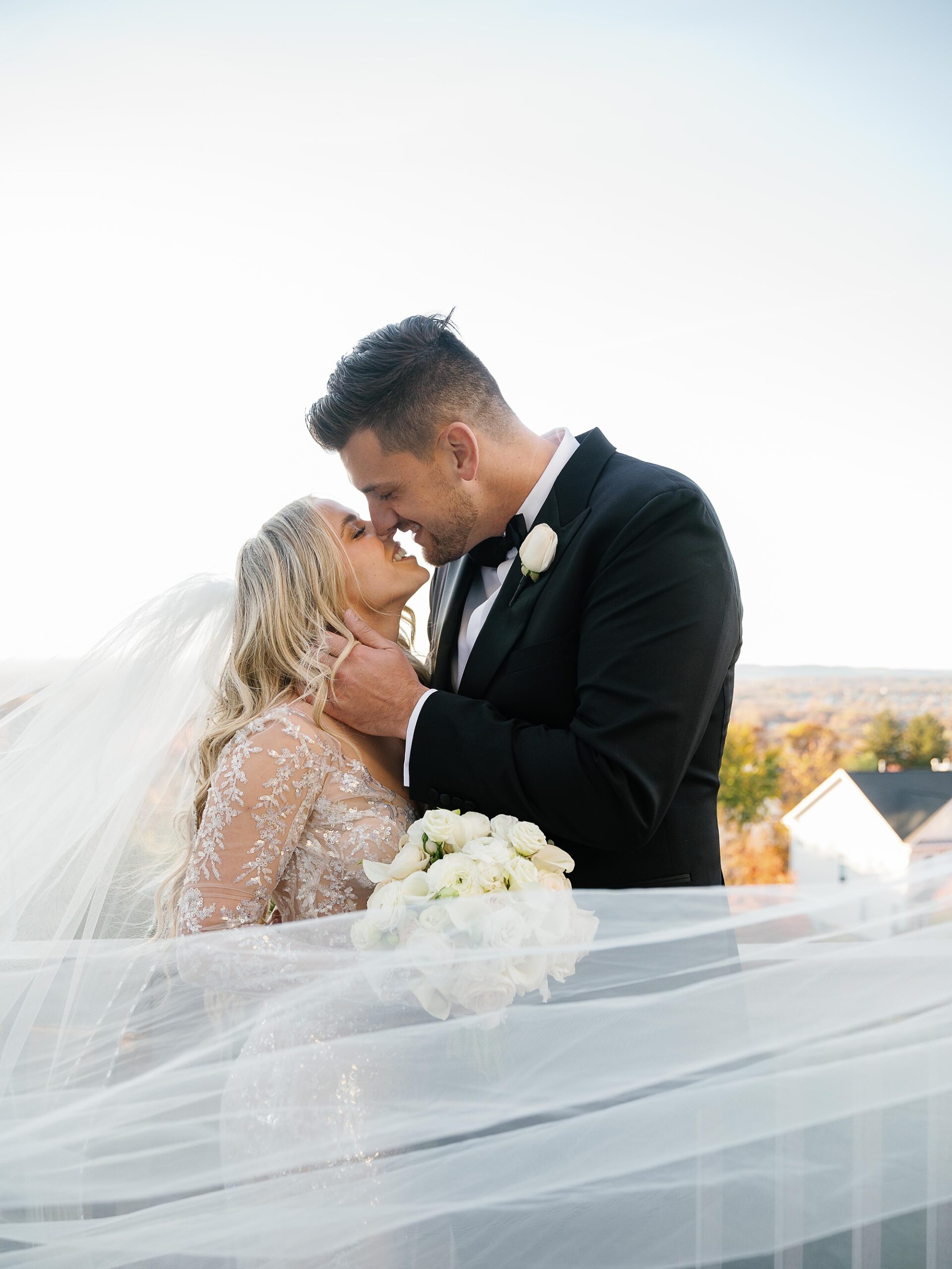 bride and groom kiss with bride's veil floating around them