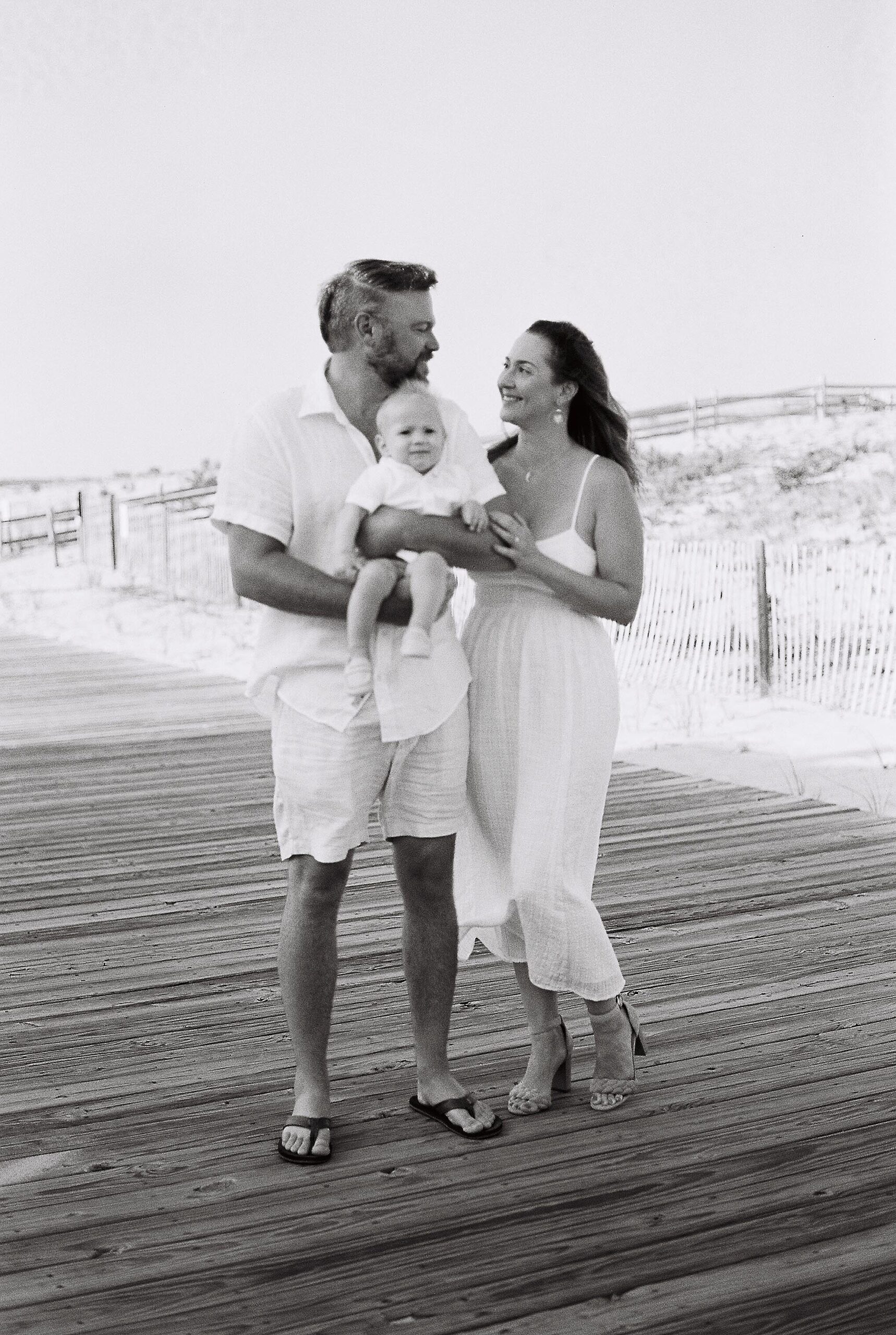 couple stands on boardwalk during first birthday portraits in Lavallette NJ