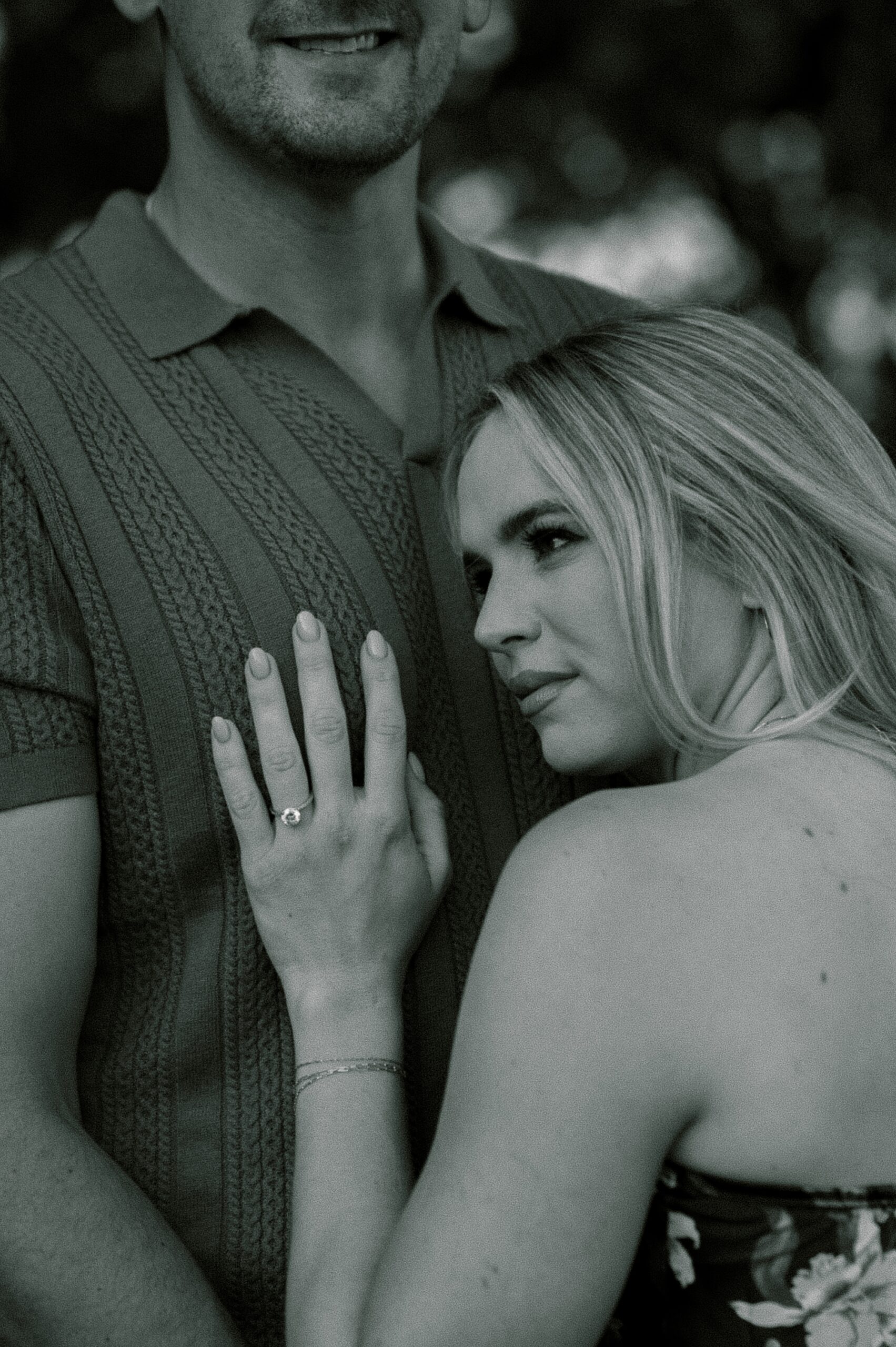 woman leans against man's chest showing off engagement ring