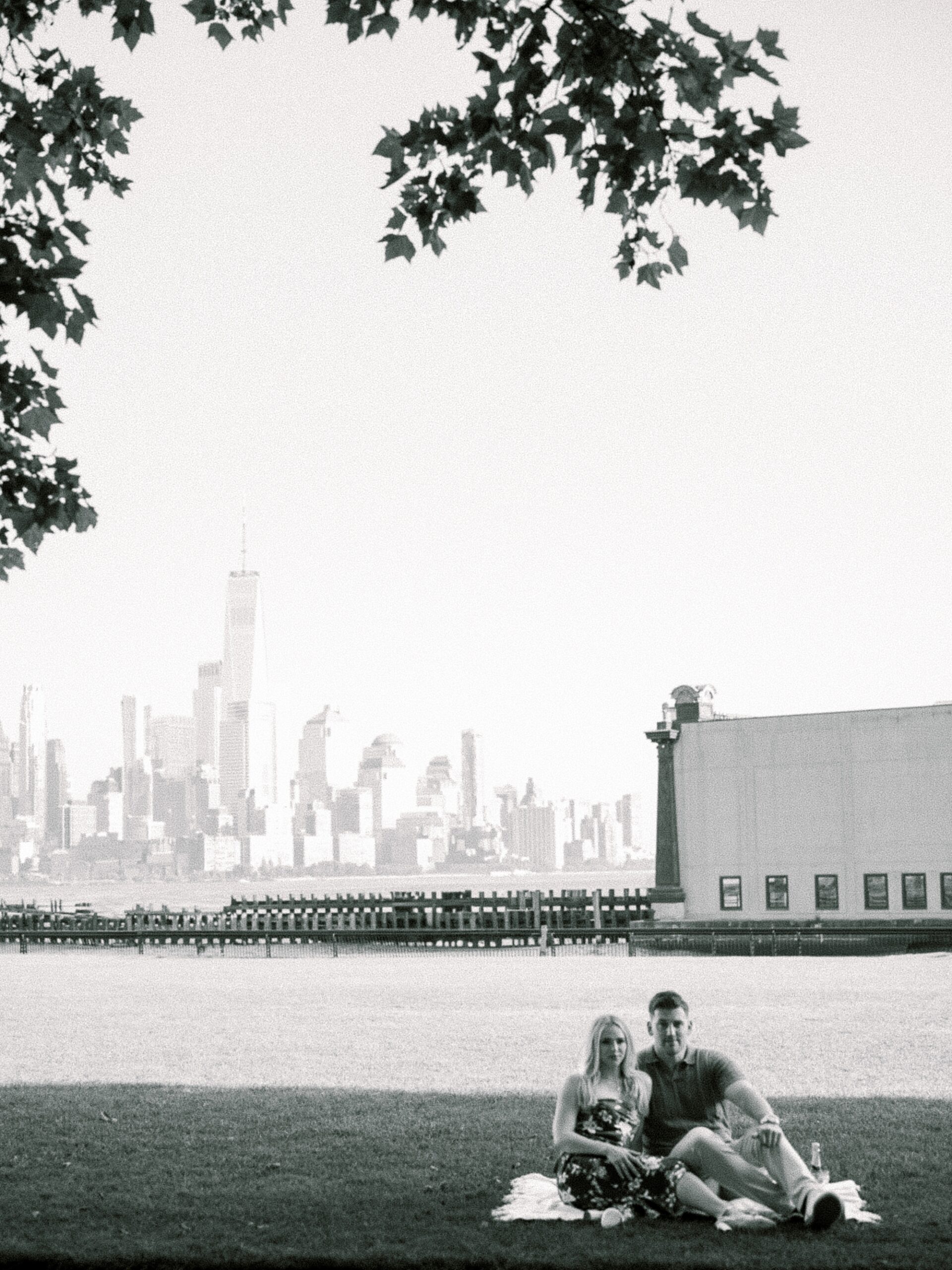 engaged couple sits on picnic blanket in front of water in Lackawanna Park