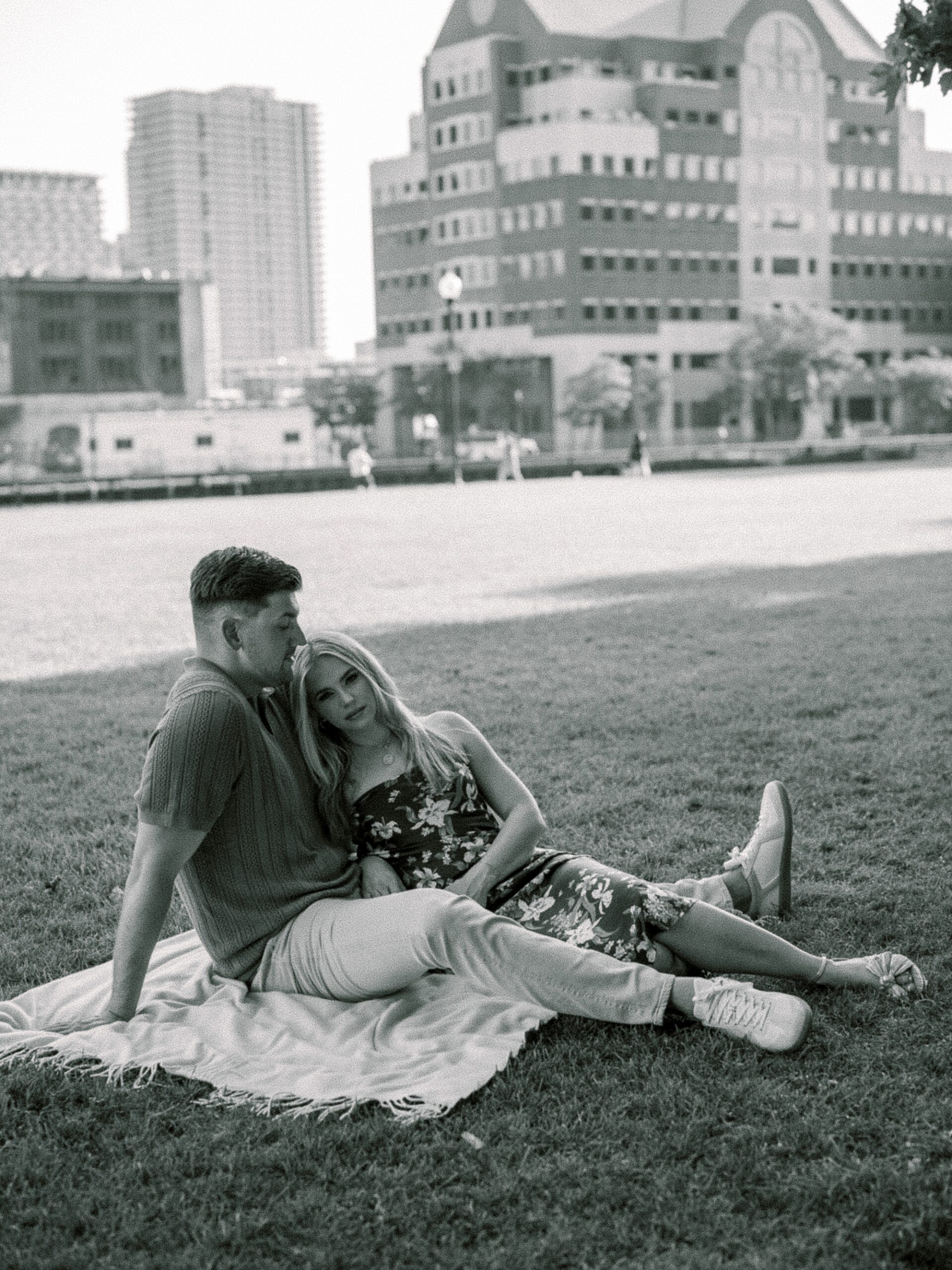 blonde woman sits between man's legs on white picnic blanket 