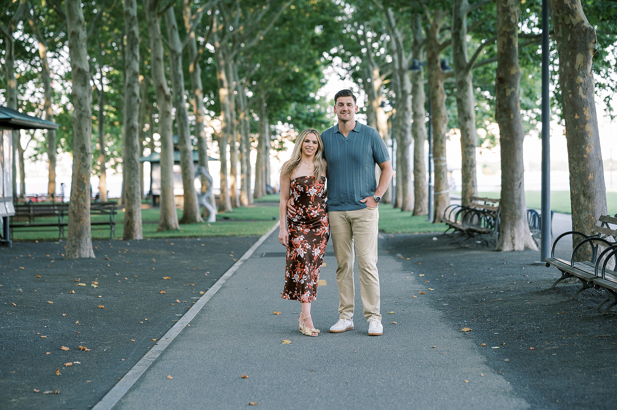 engaged couple stands on walkway between trees at Lackawanna Park