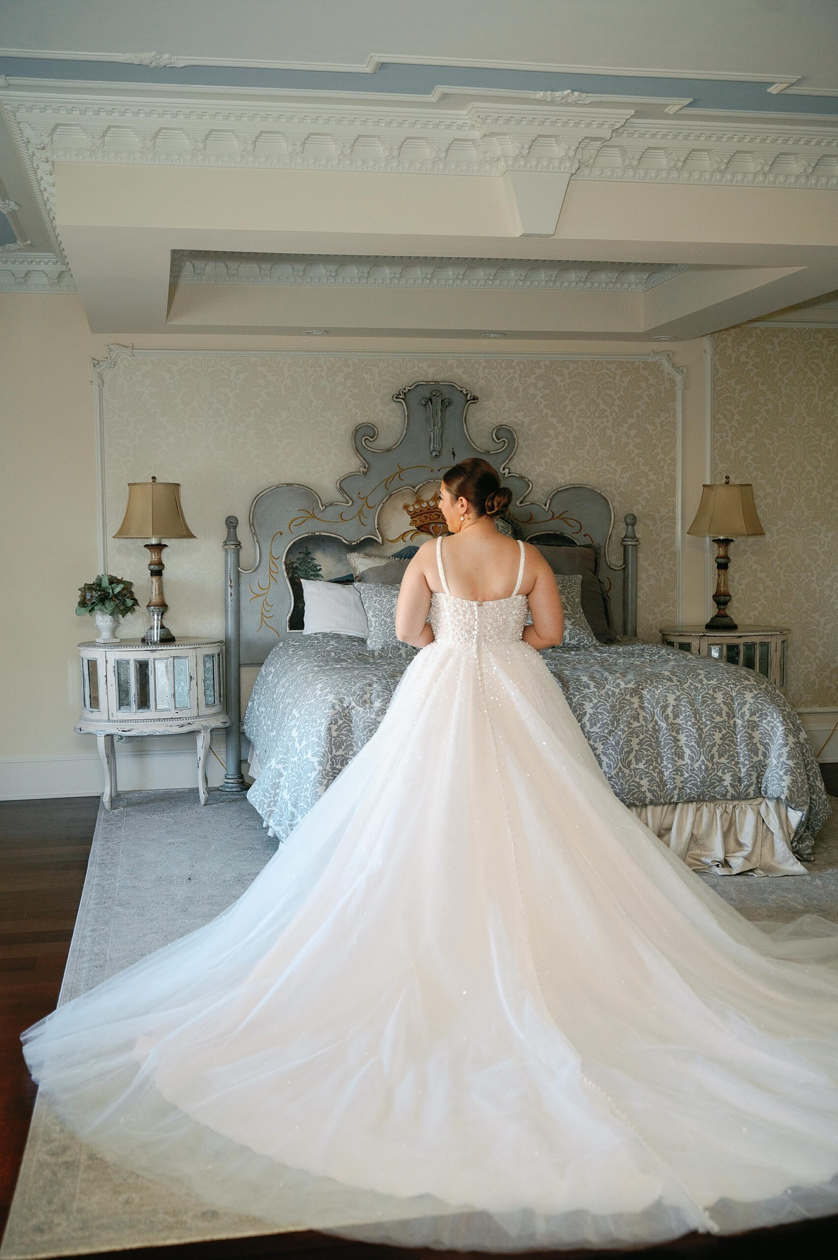 bride stands at the end of bed with dress pulled out behind her