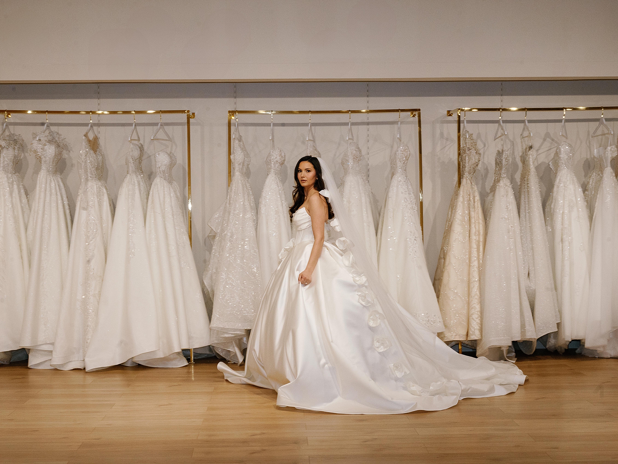 business owner walks by rack of wedding gowns during branding portraits for boutique owner