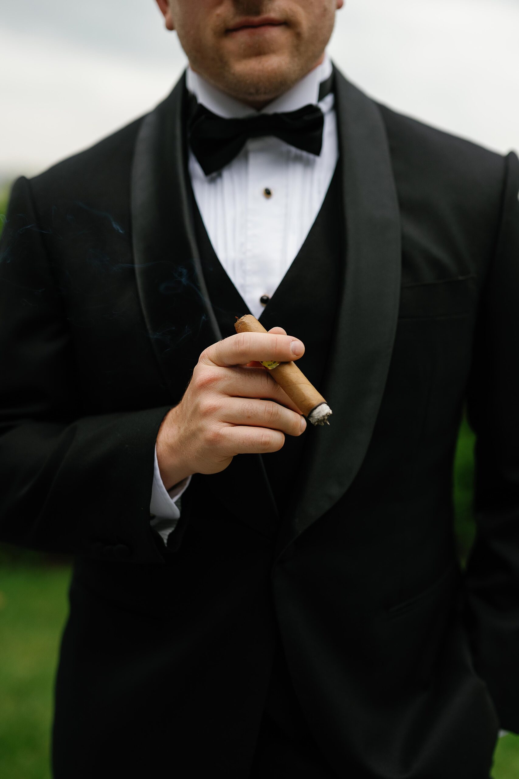 groom holds cigar in front of black suit