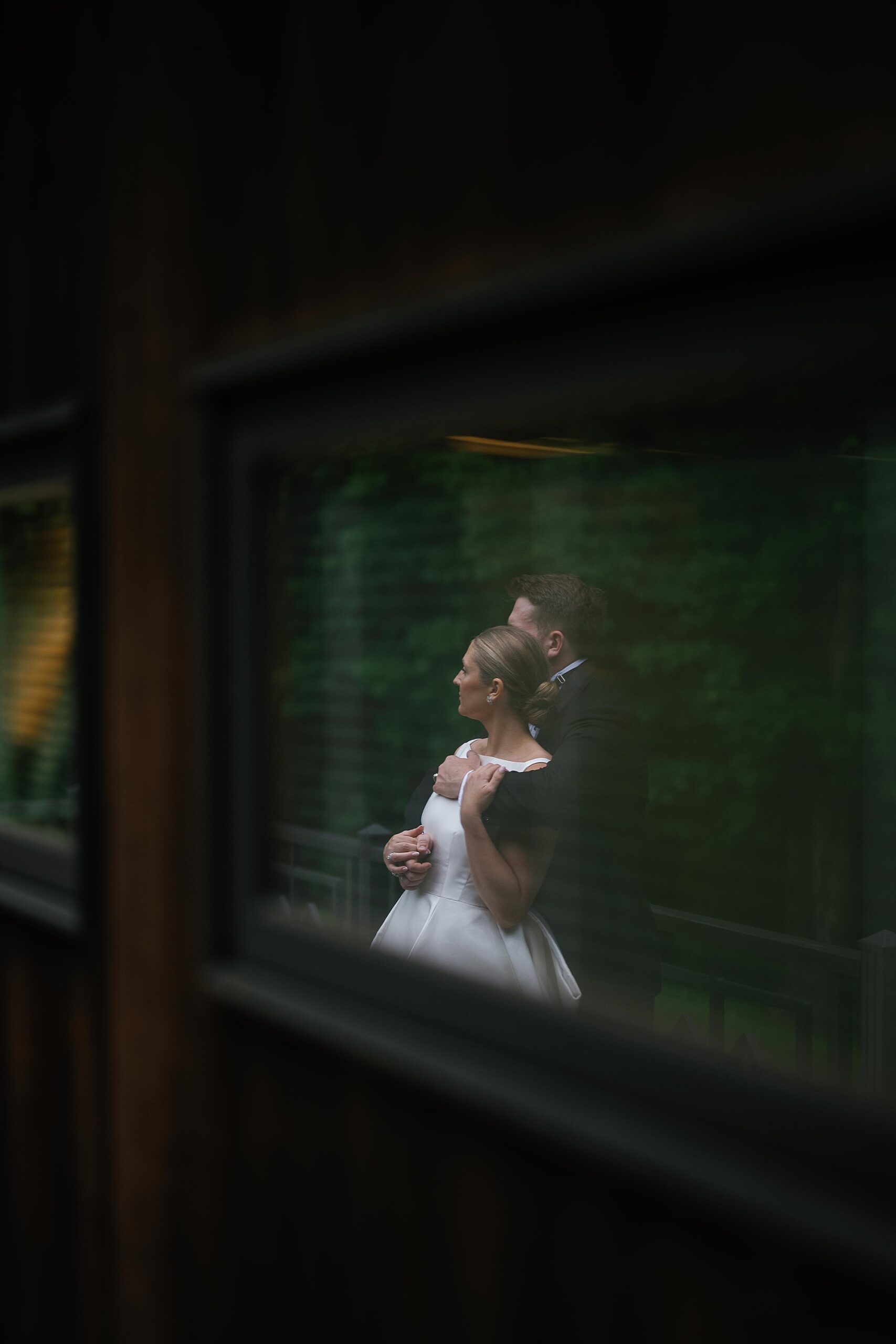 reflection of groom hugging bride from behind during rainy wedding portraits