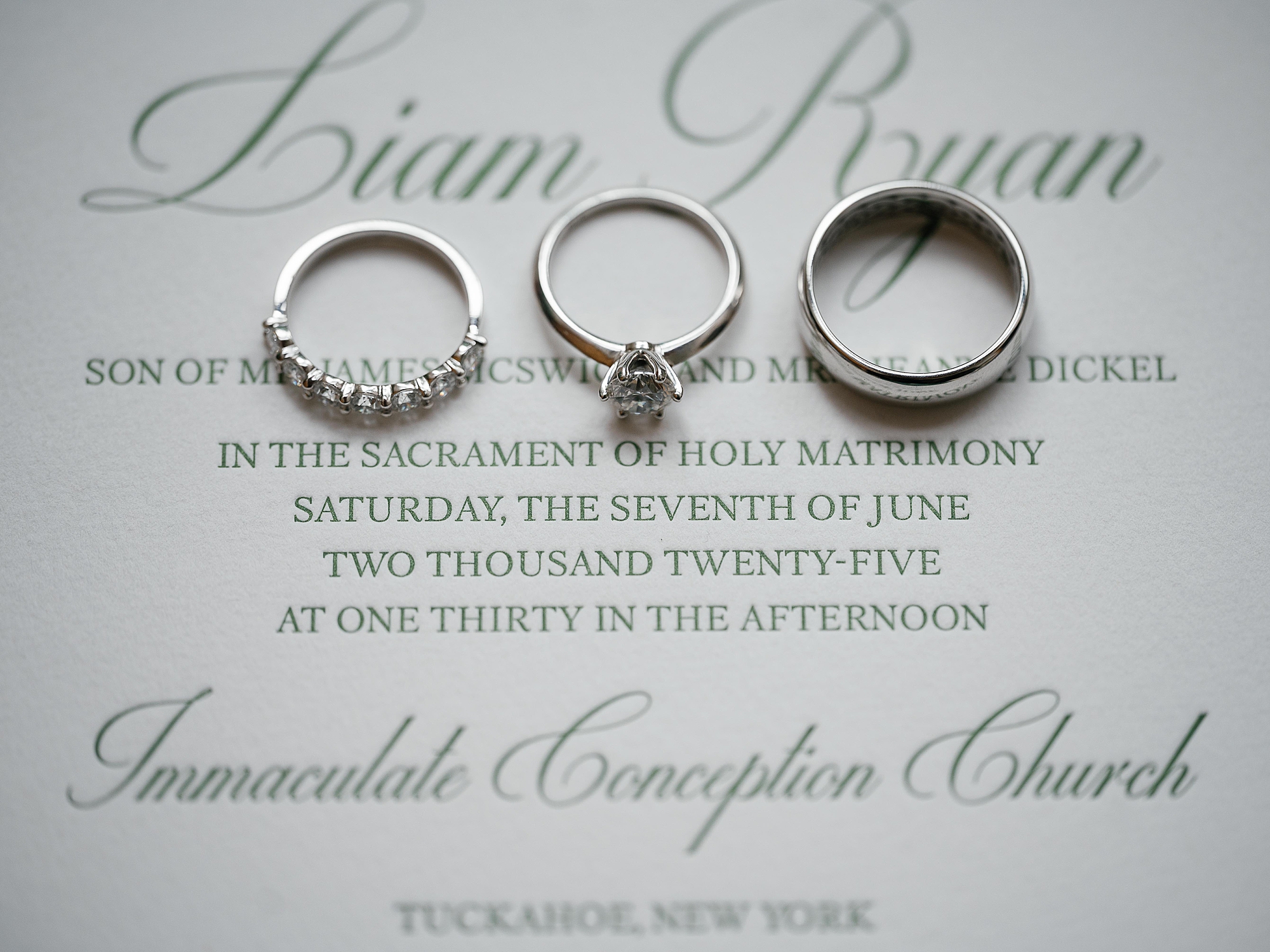 wedding rings rest on green script of invitation suite