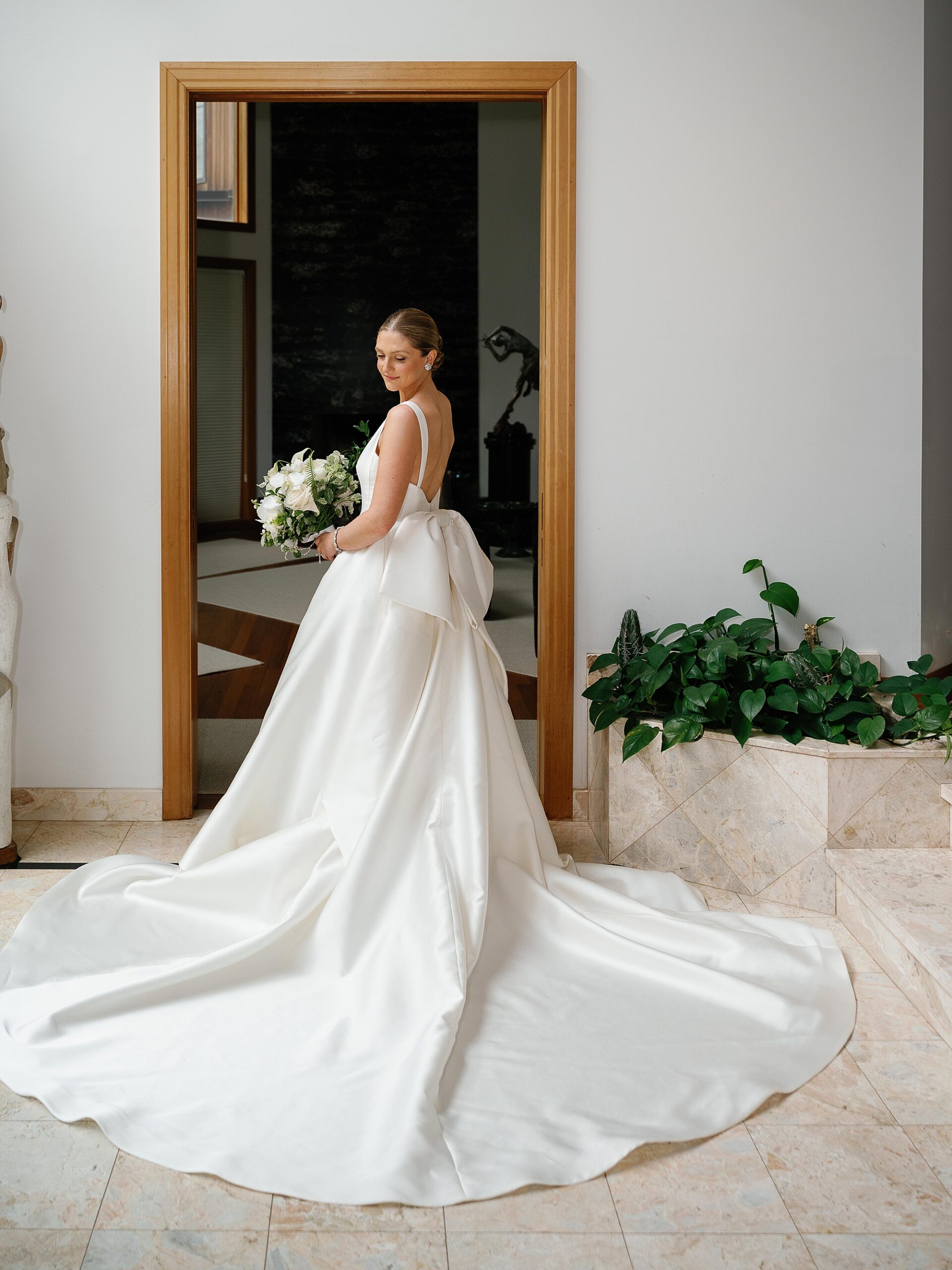 bride stands looking over shoulder holding bouquet of white roses