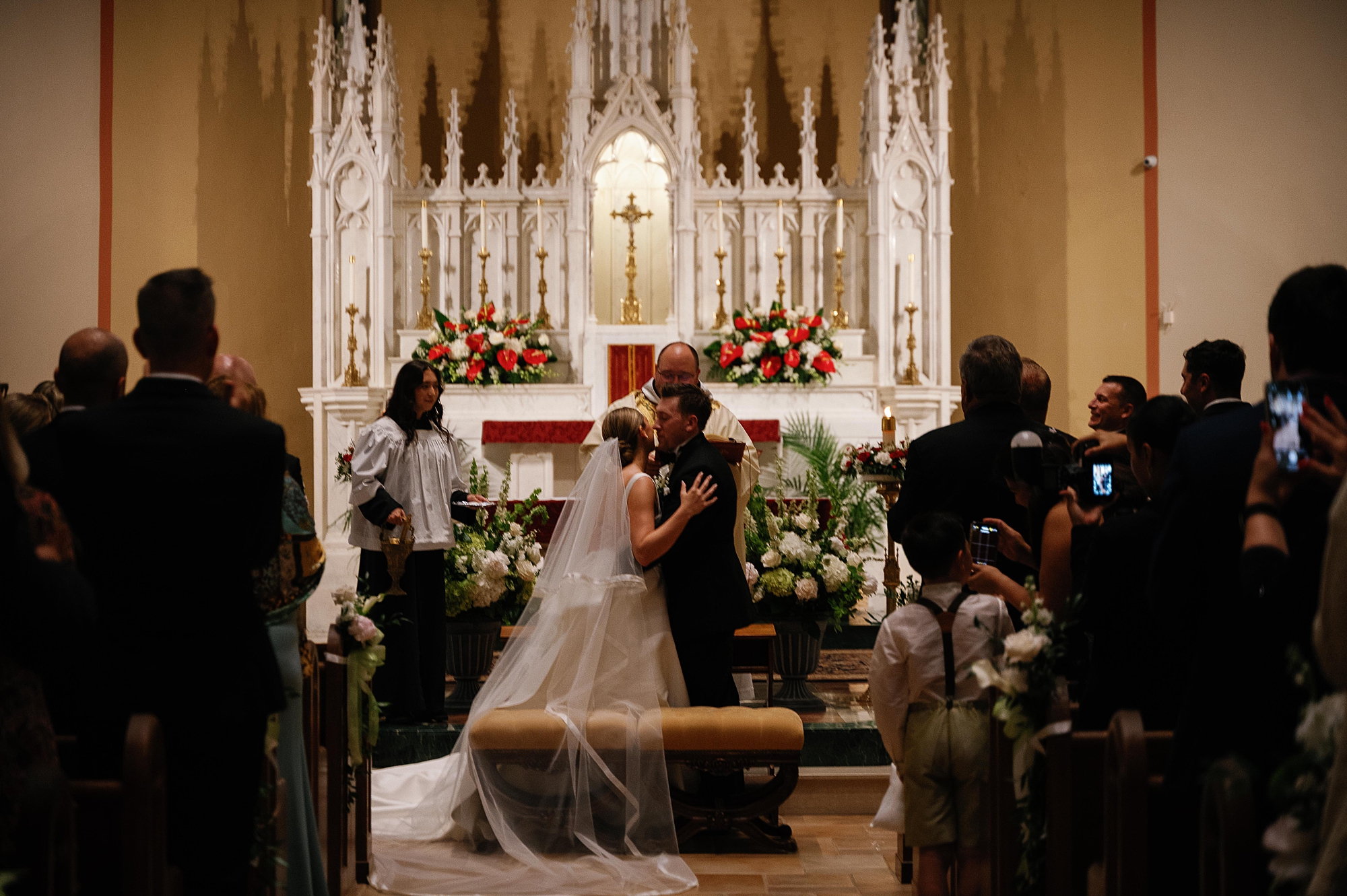 bride and groom kiss at alter at Immaculate Conception Church