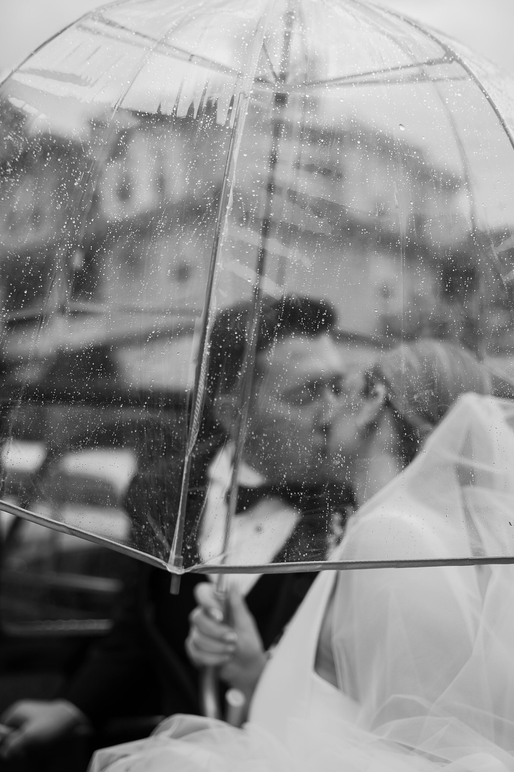 bride and groom kiss under clear umbrella on rainy wedding day