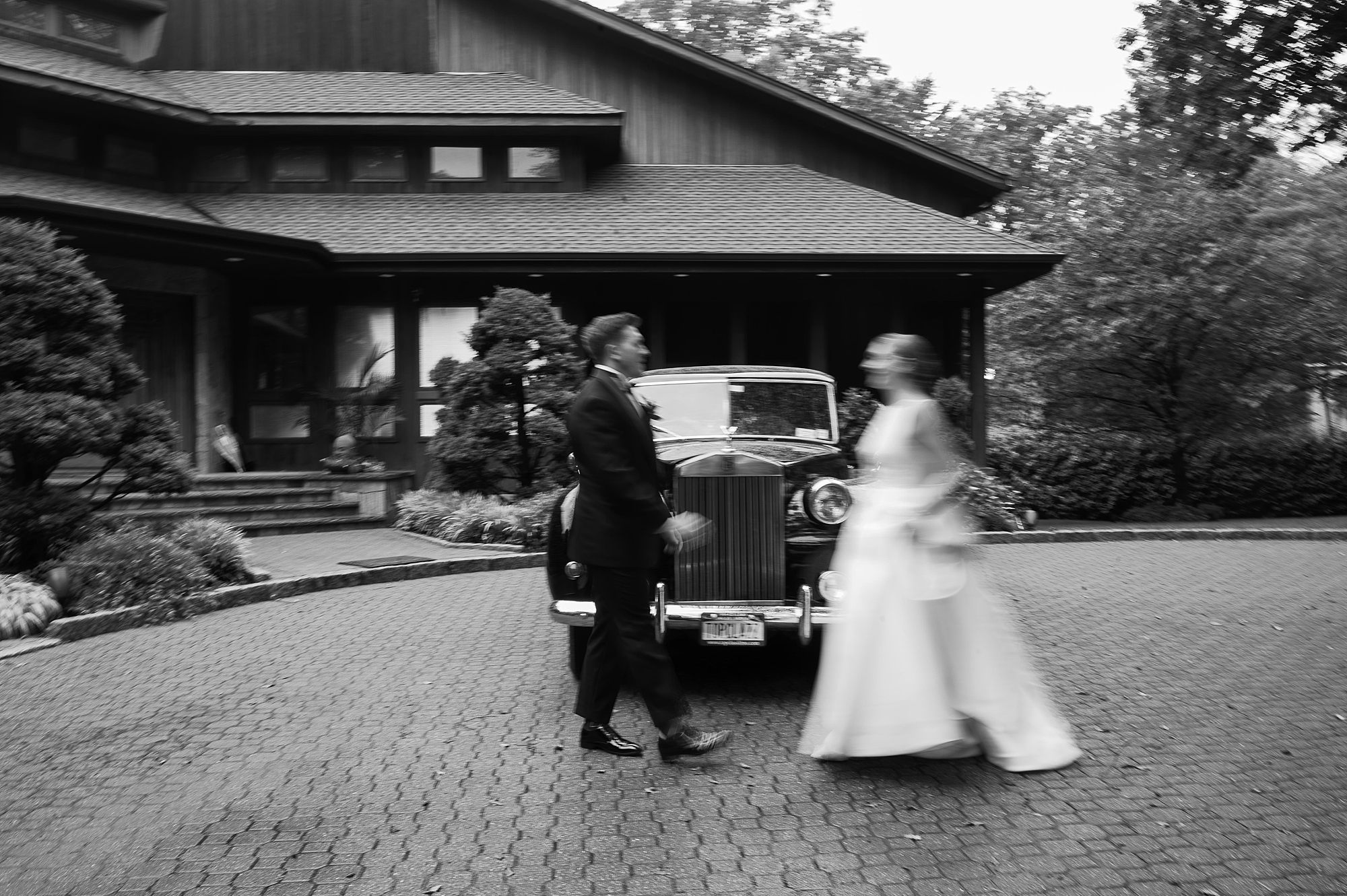 blurred motion photo of bride and groom walking near black classic car