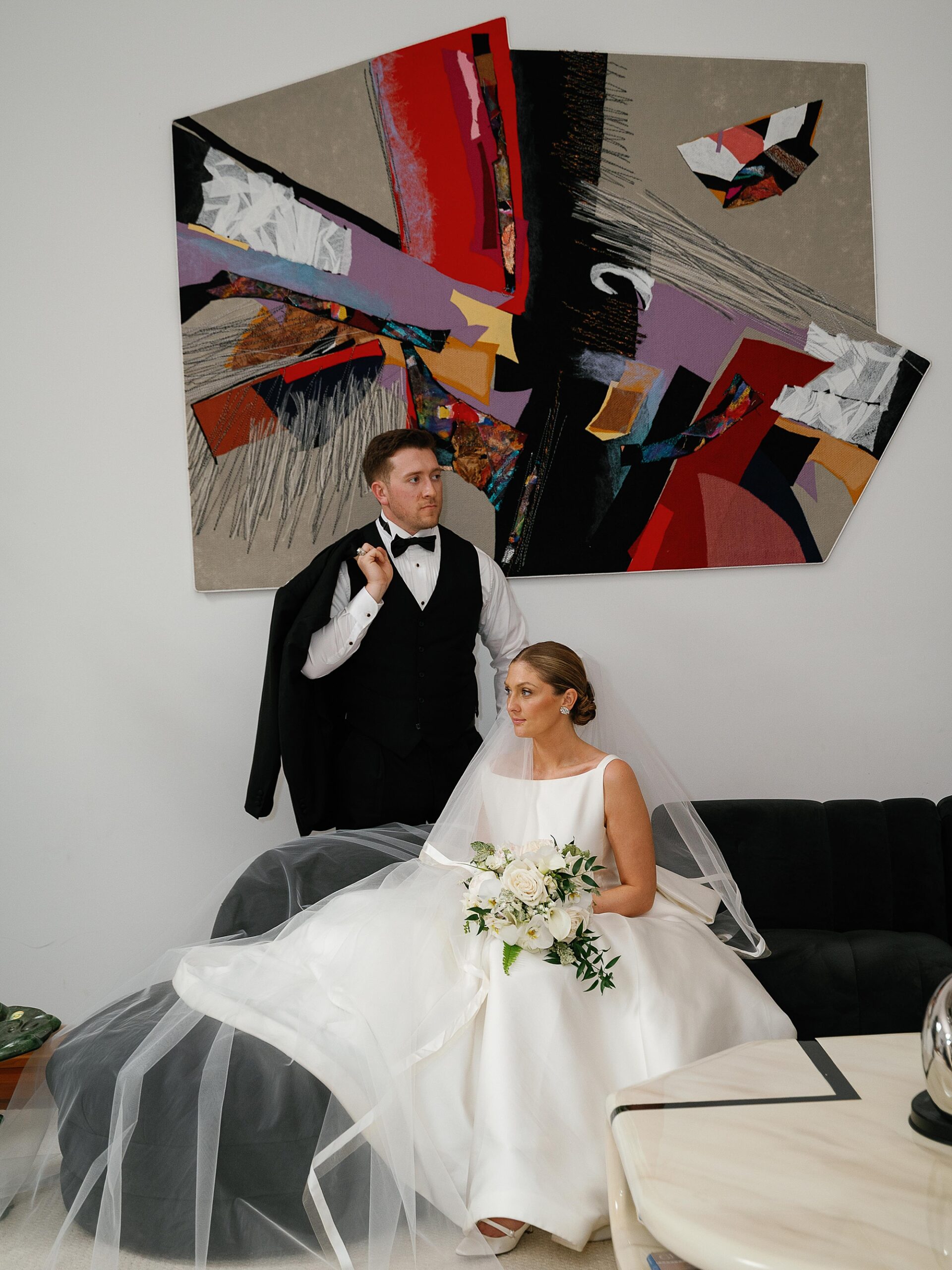 bride and groom sit on sofa under modern artwork at the Bronxville Field Club