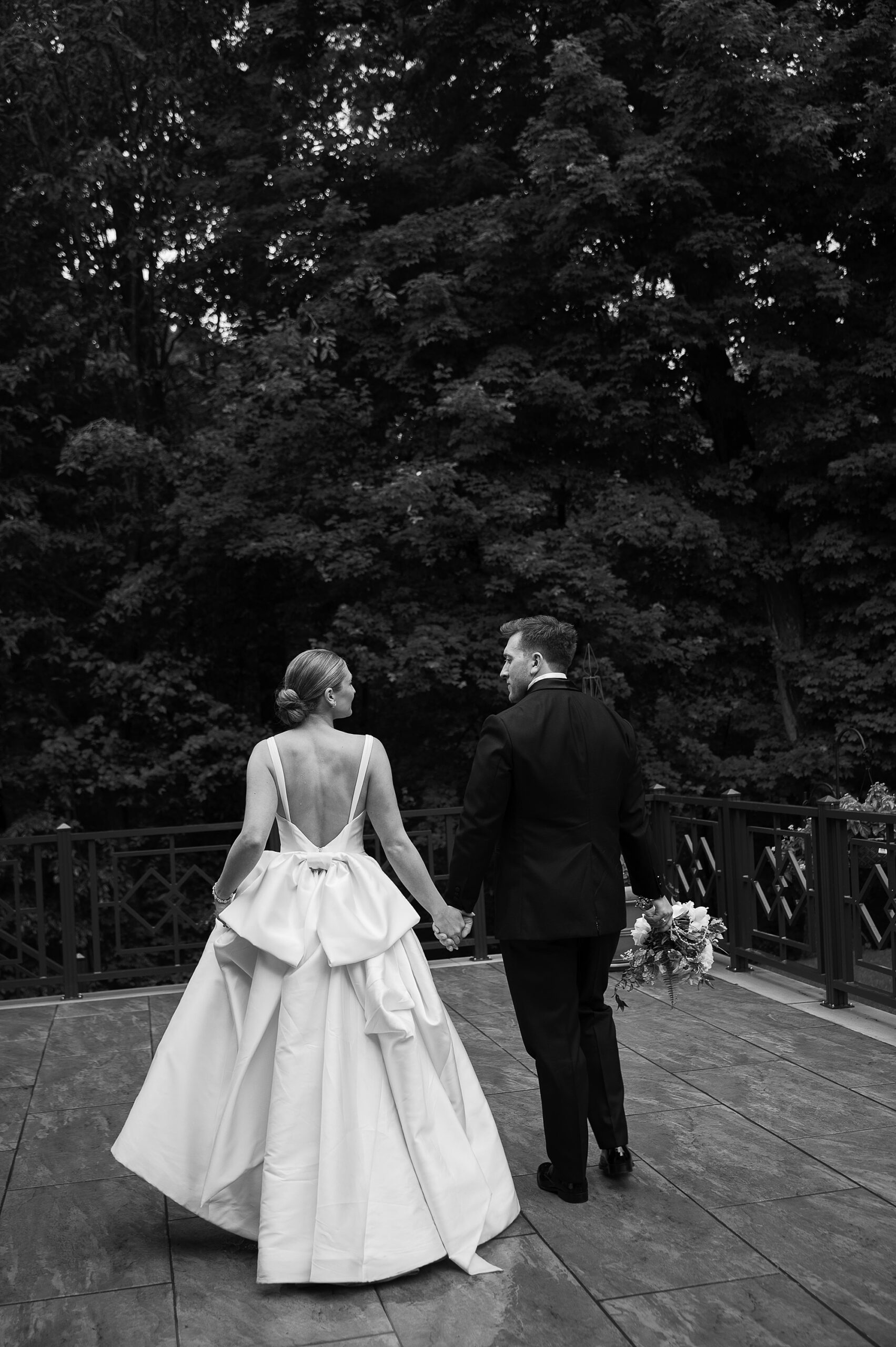 bride with bow on back of dress holds hands with groom walking at the Bronxville Field Club